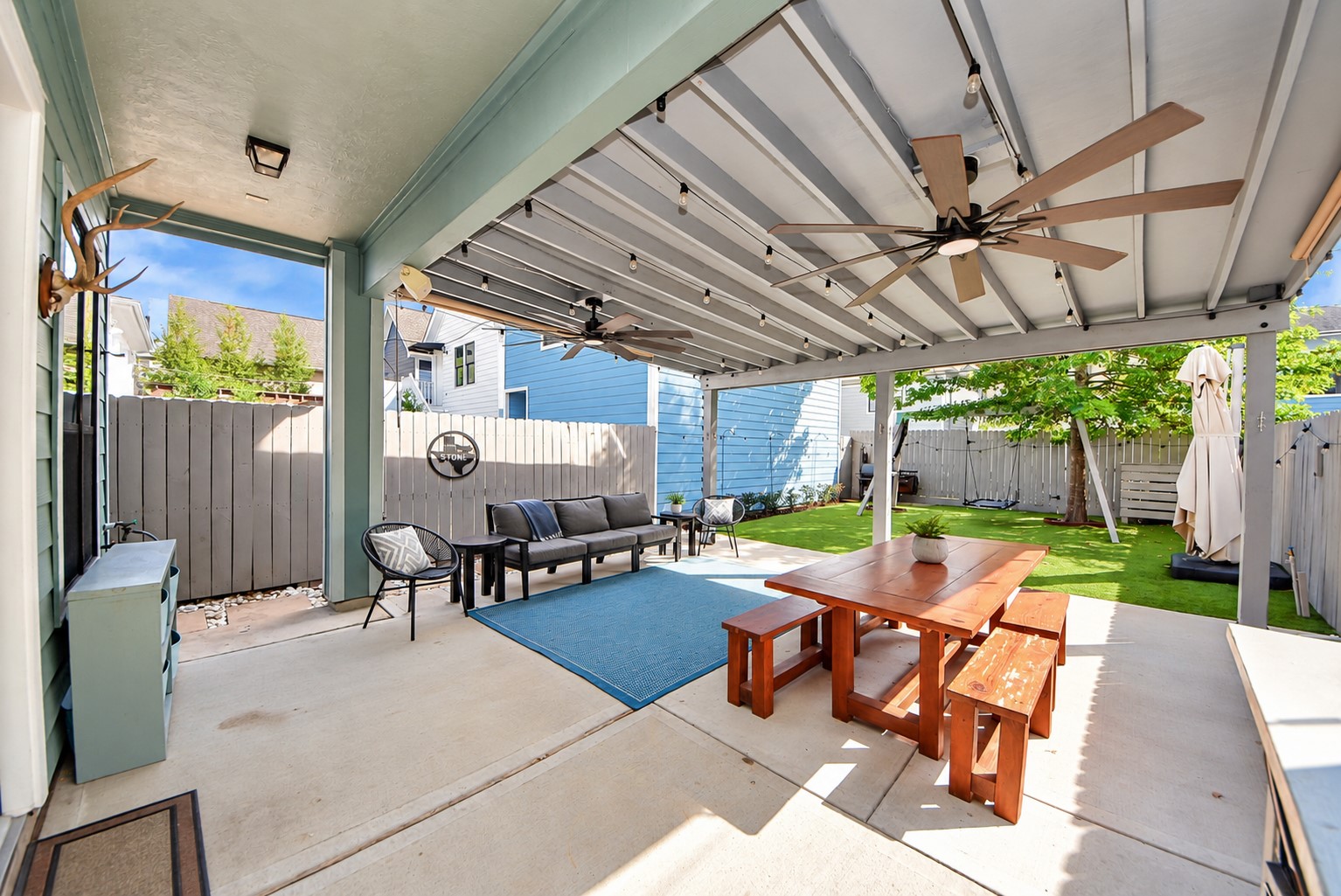 Beautiful outdoor living space featuring an expansive covered patio, ceiling fans, and a low-maintenance backyard with artificial turf. An ideal setting for gatherings, outdoor dining, and everyday enjoyment.