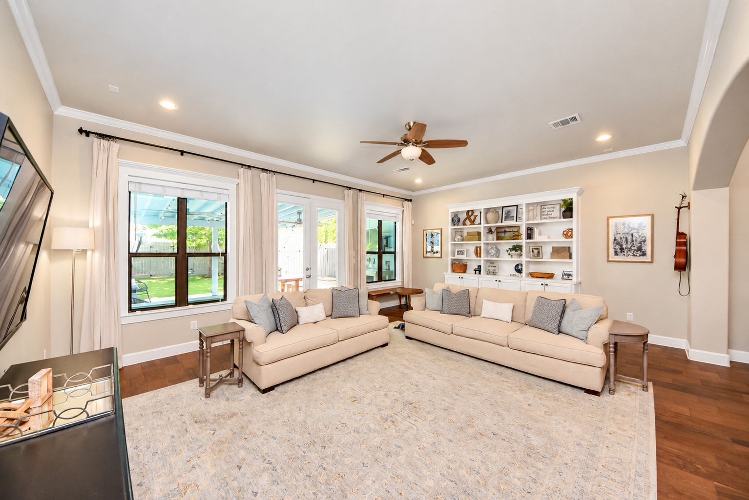 Spacious living room filled with natural light, featuring custom built-in shelving, beautiful wood floors, and backyard views.