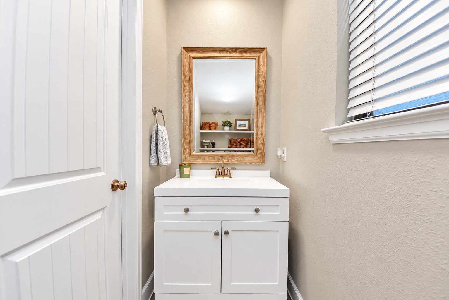 Conveniently located powder room featuring a white vanity, decorative mirror, and warm-toned fixtures.