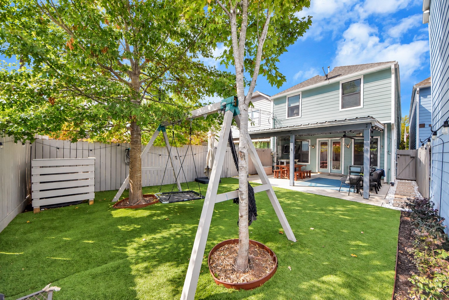Beautiful outdoor living space featuring an expansive covered patio, ceiling fans, and a low-maintenance backyard with artificial turf. An ideal setting for gatherings, outdoor dining, and everyday enjoyment.