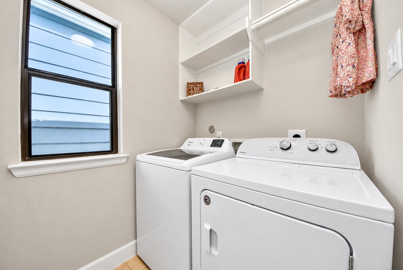 Dedicated laundry room with washer and dryer connections, overhead shelving for additional storage, and a window that welcomes natural light.