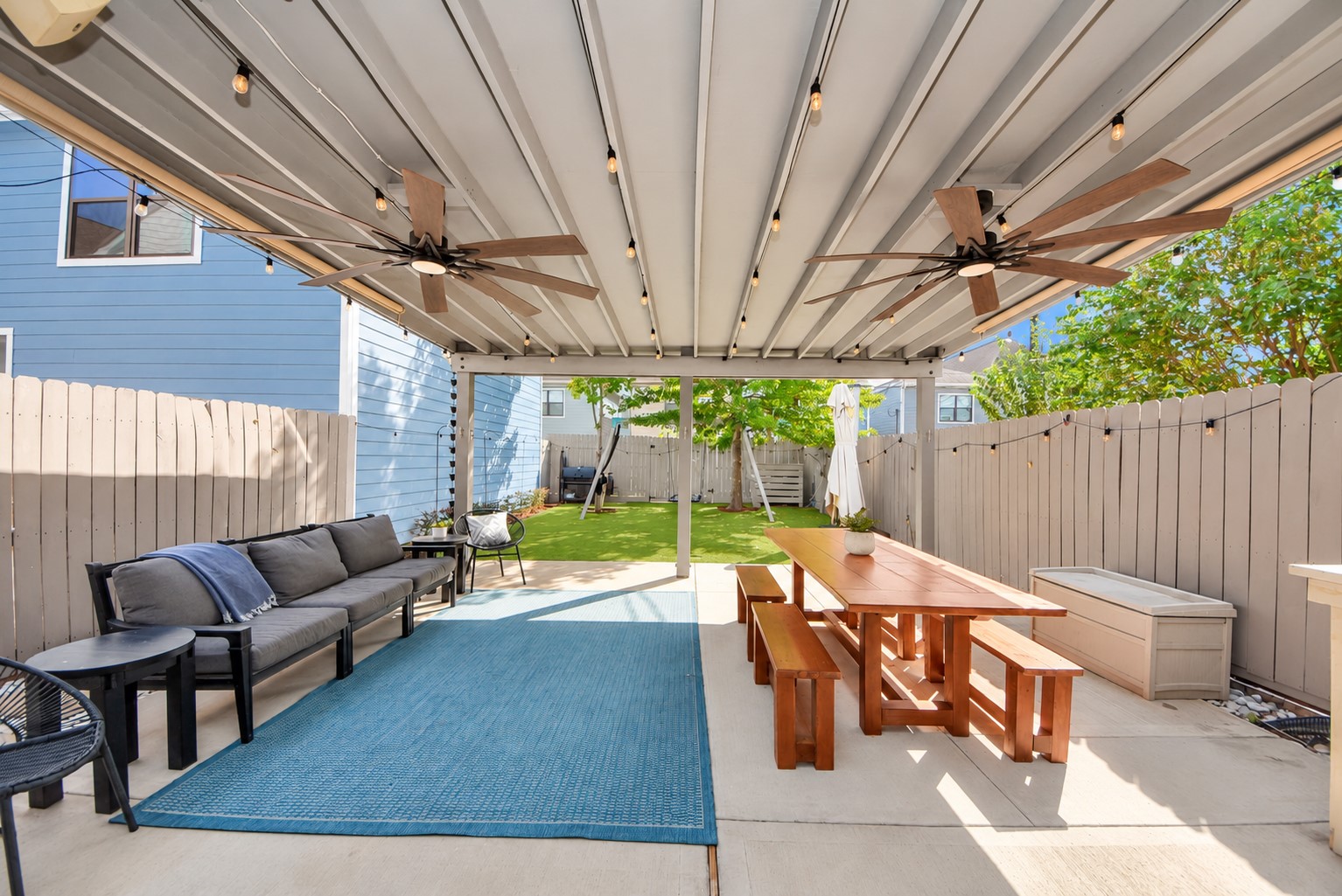 Beautiful outdoor living space featuring an expansive covered patio, ceiling fans, and a low-maintenance backyard with artificial turf. An ideal setting for gatherings, outdoor dining, and everyday enjoyment.