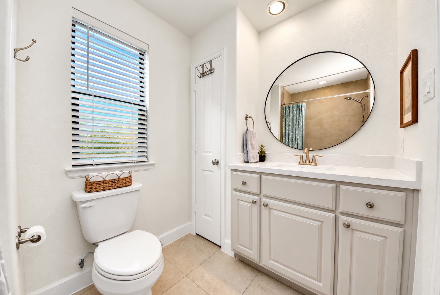 Bright secondary bathroom featuring a spacious vanity with generous countertop space, stylish round mirror, updated fixtures, and natural light.