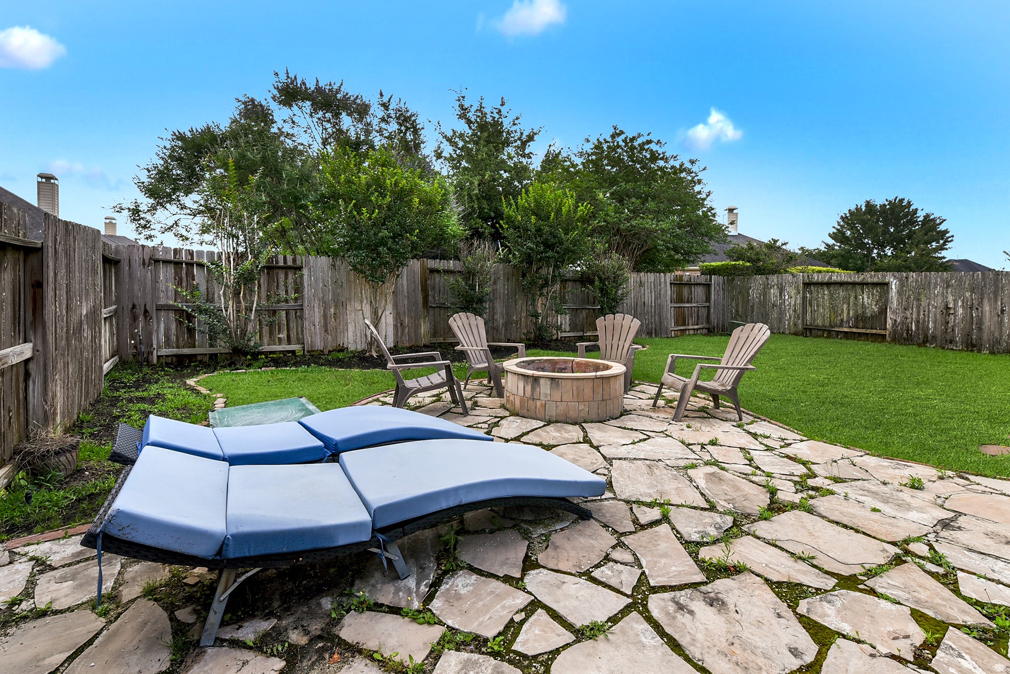 A view of the stone patio with a firepit showcases a charming outdoor space ideal for gathering around the fire and enjoying the ambiance of the backyard.
