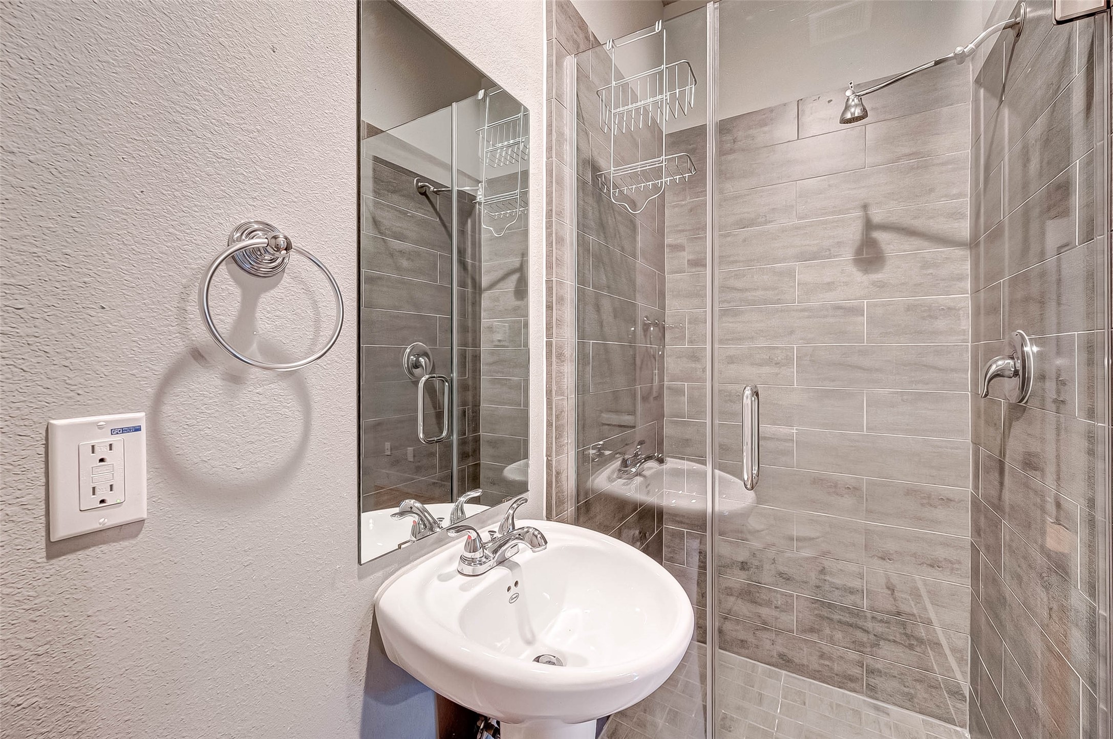 Modern bathroom featuring a sleek glass-enclosed shower with stylish gray tile, complemented by a chic pedestal sink and contemporary fixtures.