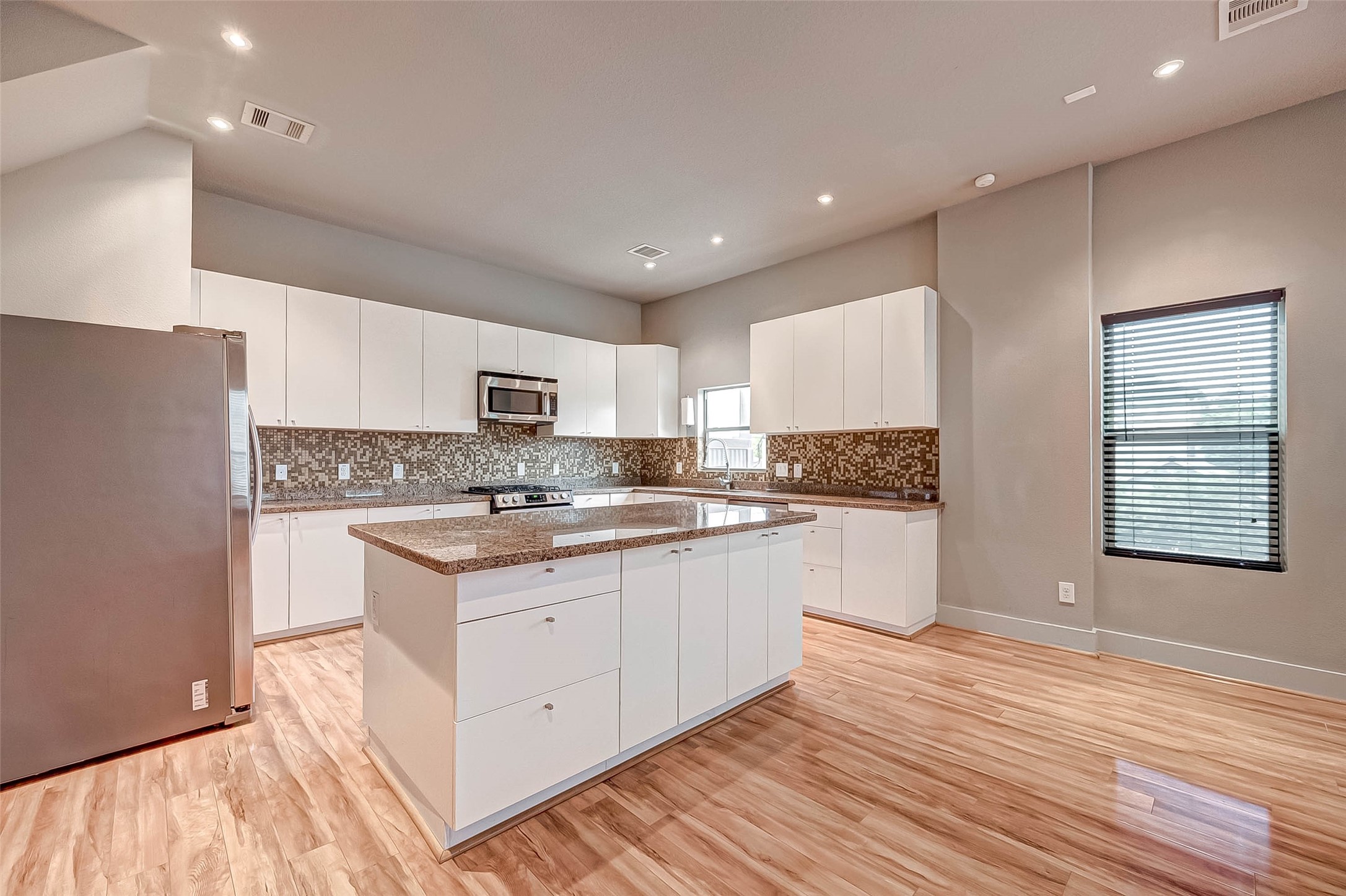 Modern kitchen with sleek white cabinetry, stainless steel appliances, and a stylish mosaic tile backsplash. A central island offers additional workspace, while the light wood flooring adds warmth to the space.
