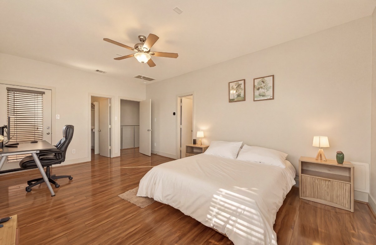 Spacious bedroom featuring warm hardwood floors, a cozy bed with stylish side tables, and a convenient workspace with a modern desk.