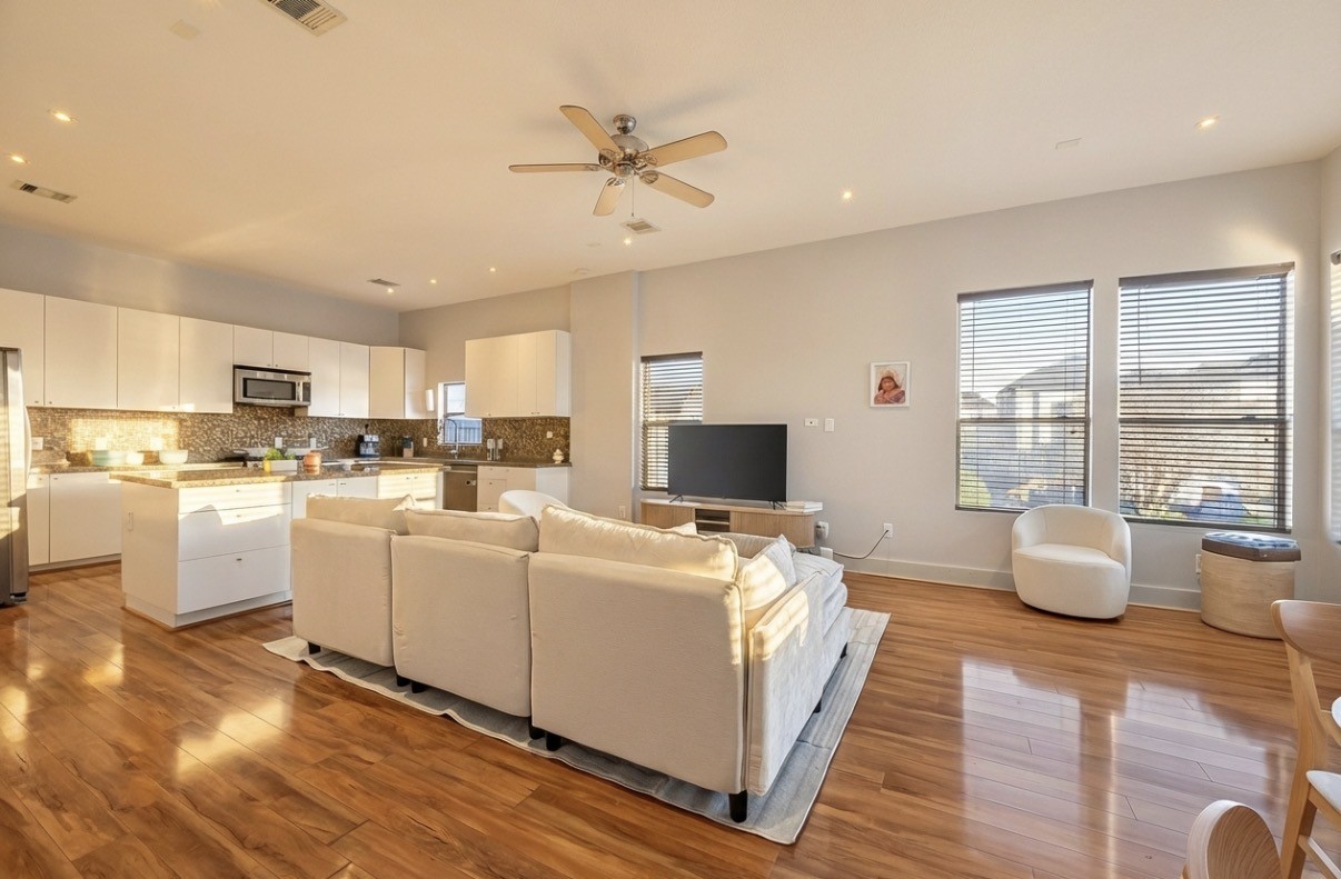 Spacious open-concept living area with warm wood flooring, modern kitchen cabinetry, and large windows offering ample natural light.