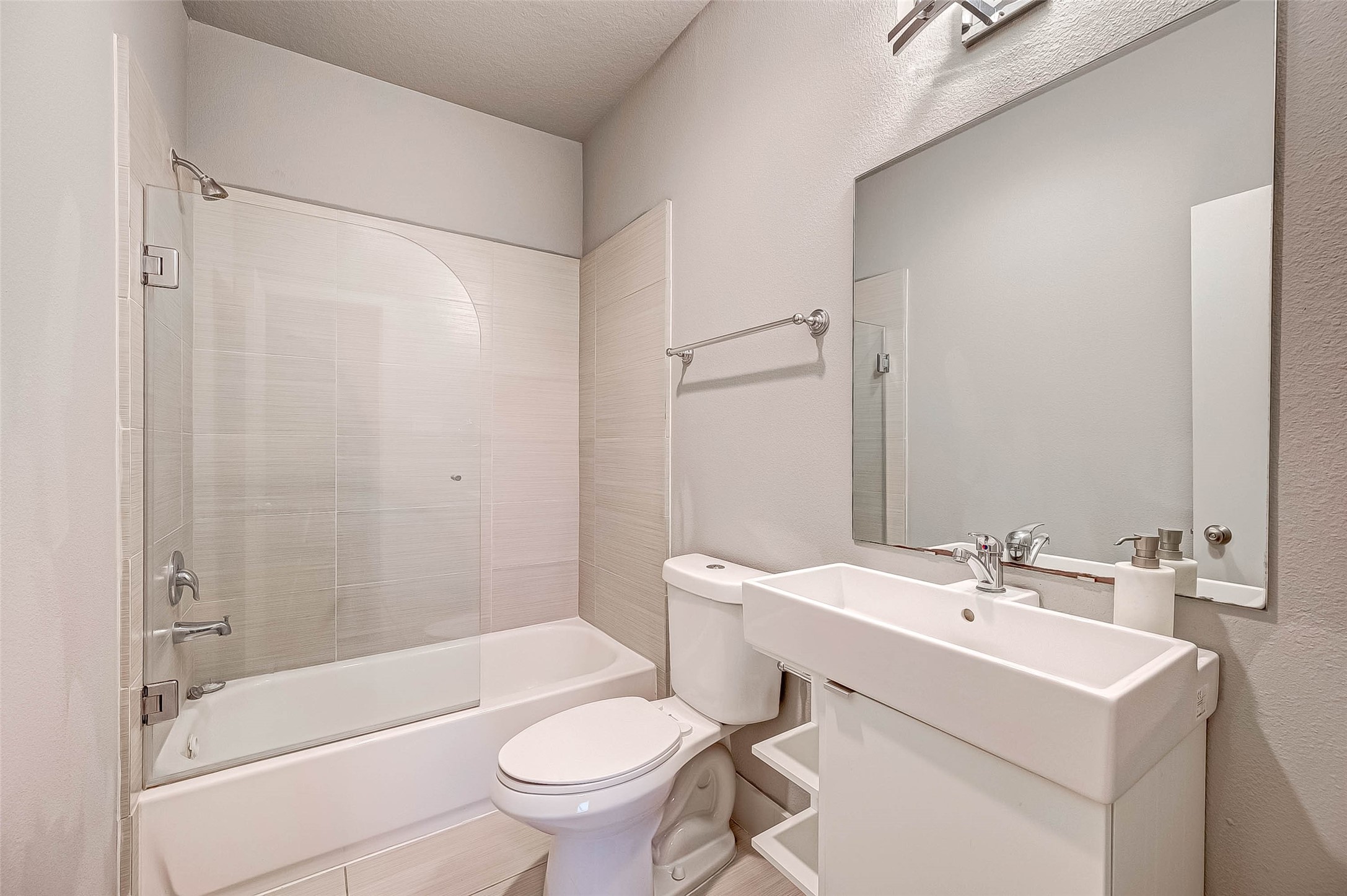 Modern bathroom featuring a sleek tub-shower combo, contemporary sink, and ample mirror space, all in a bright, neutral palette.