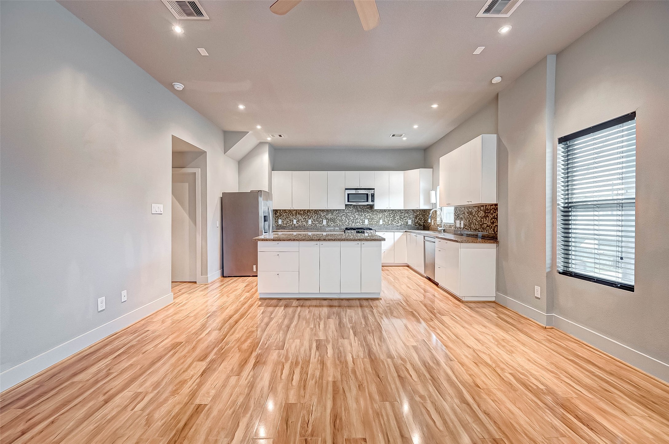 Spacious open-concept kitchen with modern white cabinetry, stainless steel appliances, and elegant wood flooring, perfect for entertaining and daily living.