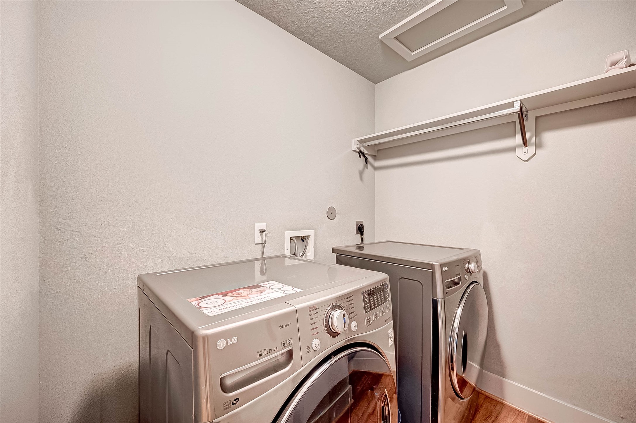 Modern laundry room with sleek LG washer and dryer, wood flooring, and a convenient overhead shelf for storage.