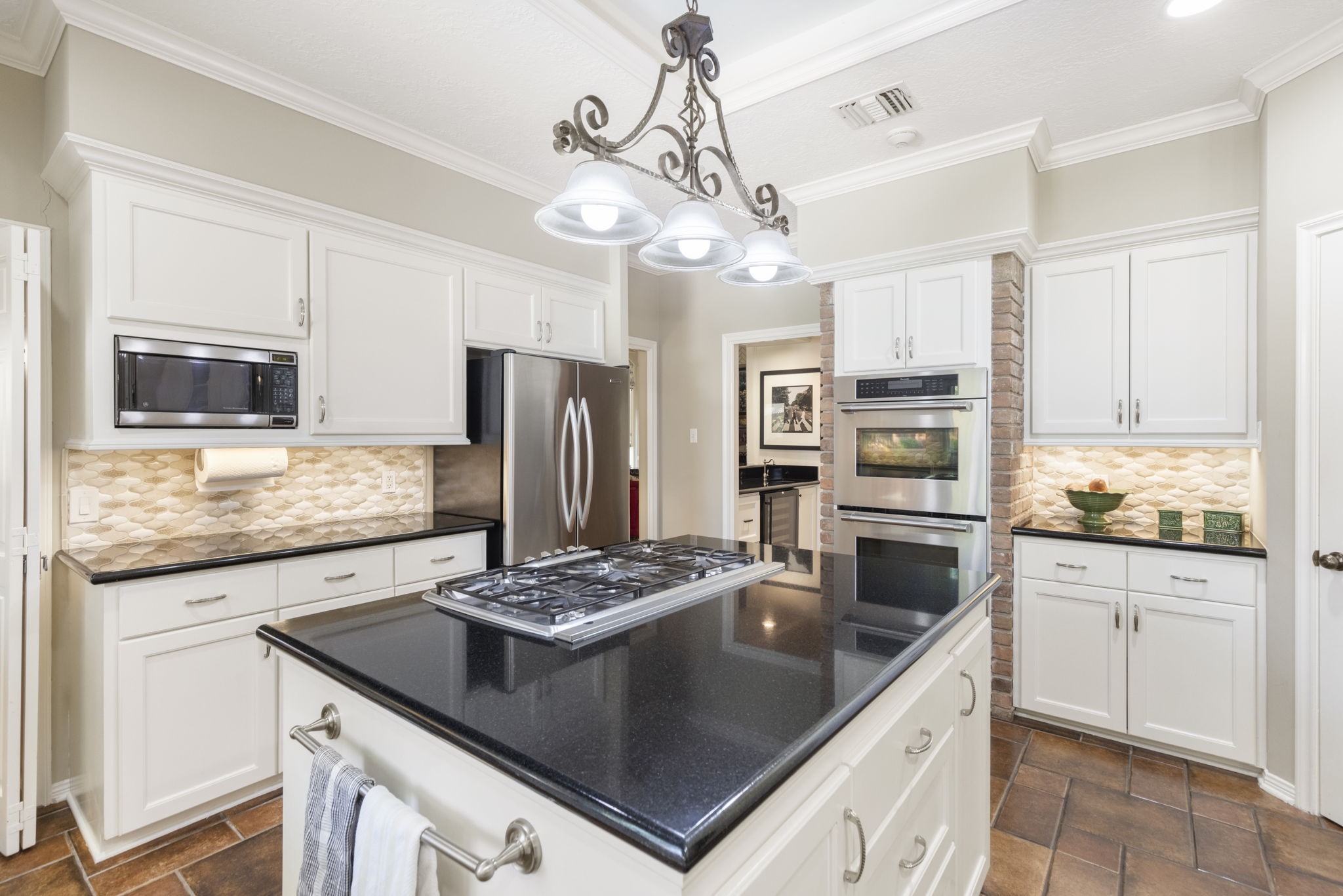 White cabinetry, dark counters, a gas cooktop island, and double wall ovens create a kitchen ready for everyday meals and ambitious entertaining.