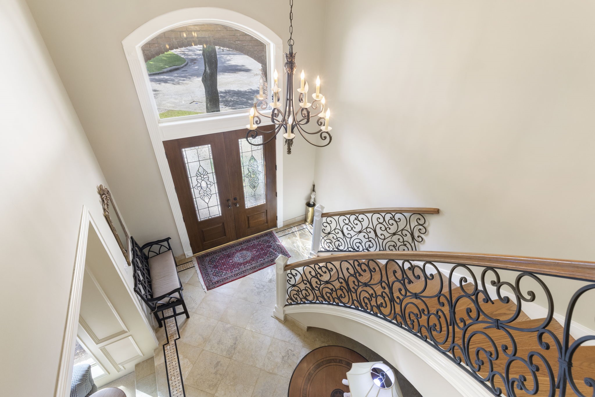 Viewed from above, the dramatic foyer showcases graceful curves, intricate ironwork, and an arched window that welcomes natural light.