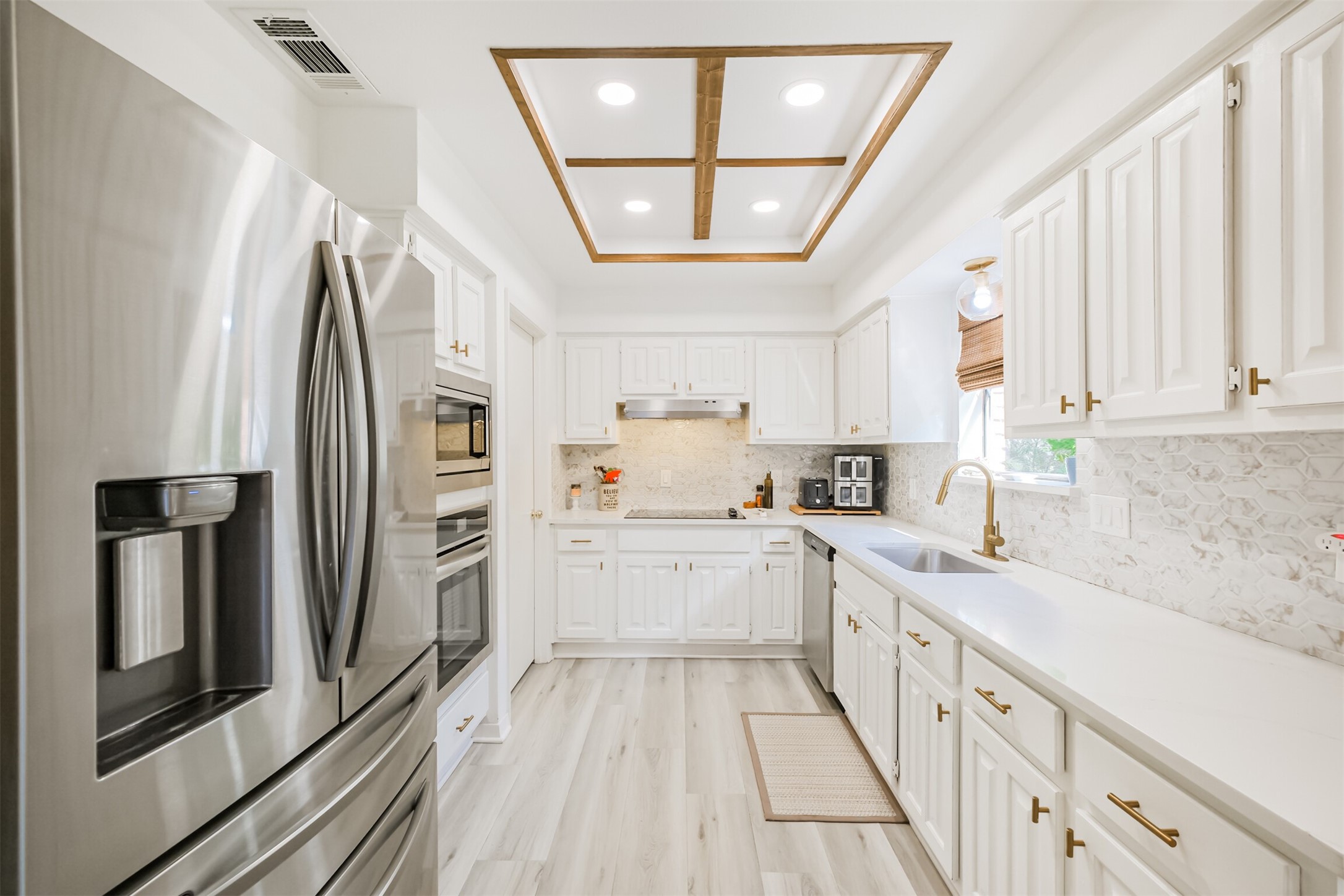 There are quartz counters with tile backsplash, gold fixtures and stainless steel appliances in the kitchen.