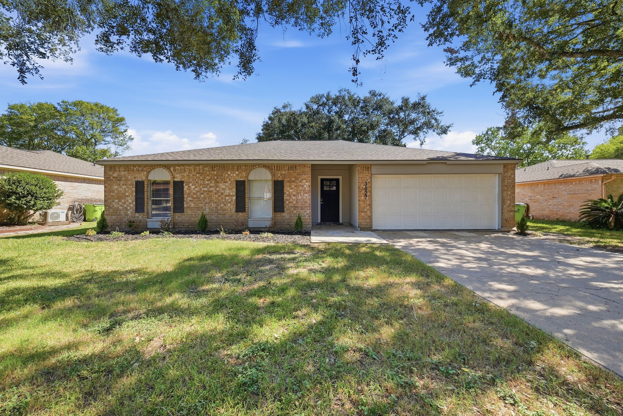 Brick single-story home under mature oaks with a wide driveway and attached two-car garage.