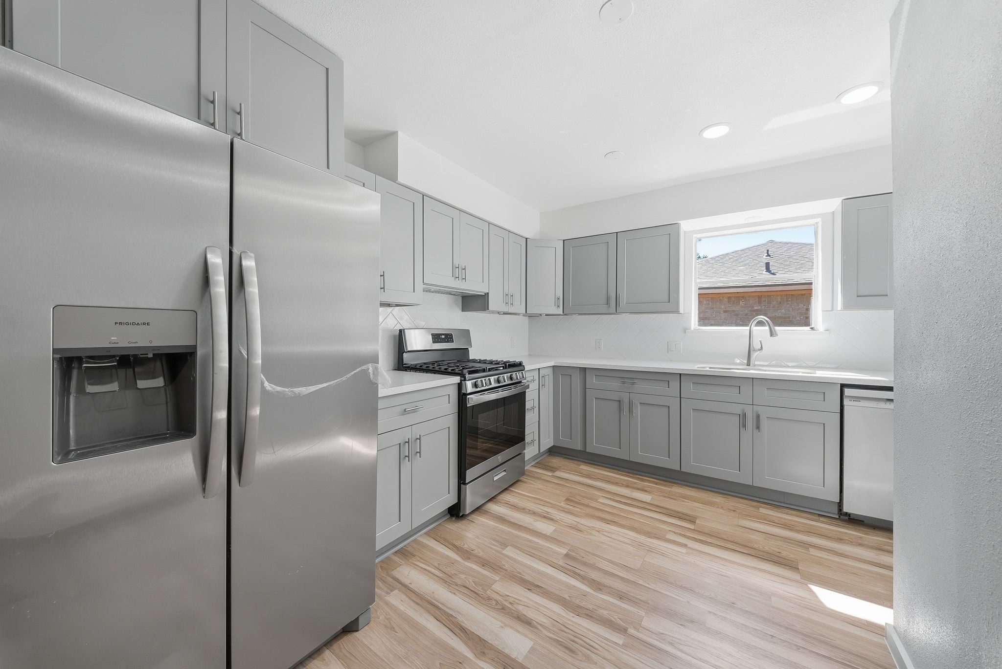 Cook on a gas range with gray shaker cabinets, stainless appliances and a window over the sink.