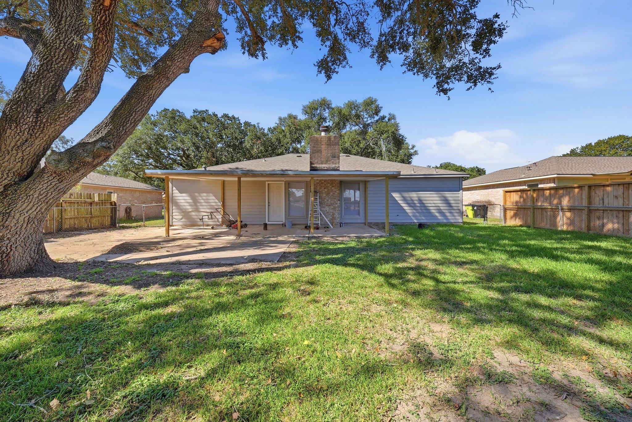 Fenced backyard with a covered patio, a brick chimney and plenty of lawn.