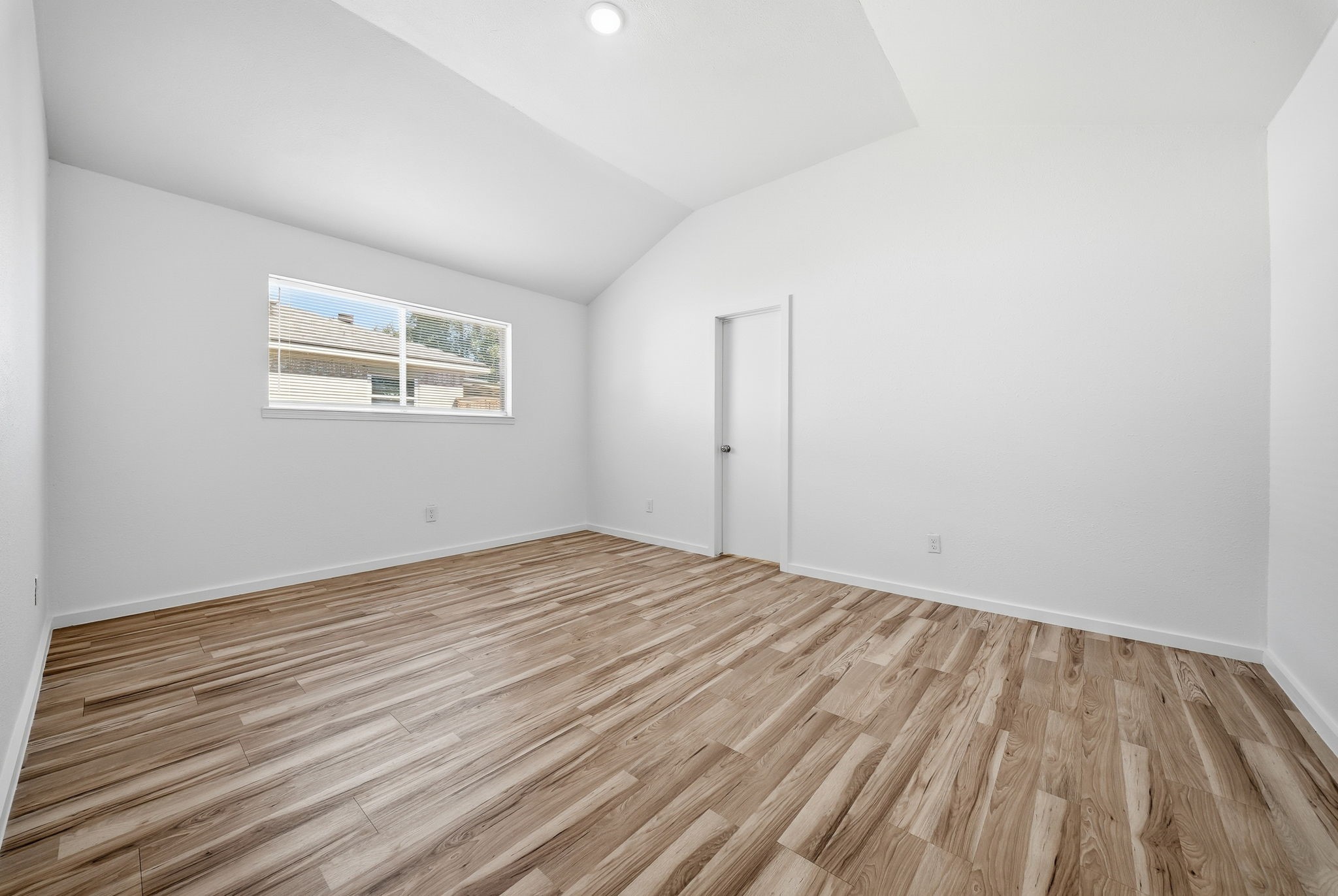 Primary bedroom shown empty, with a vaulted ceiling and wood-look floors.