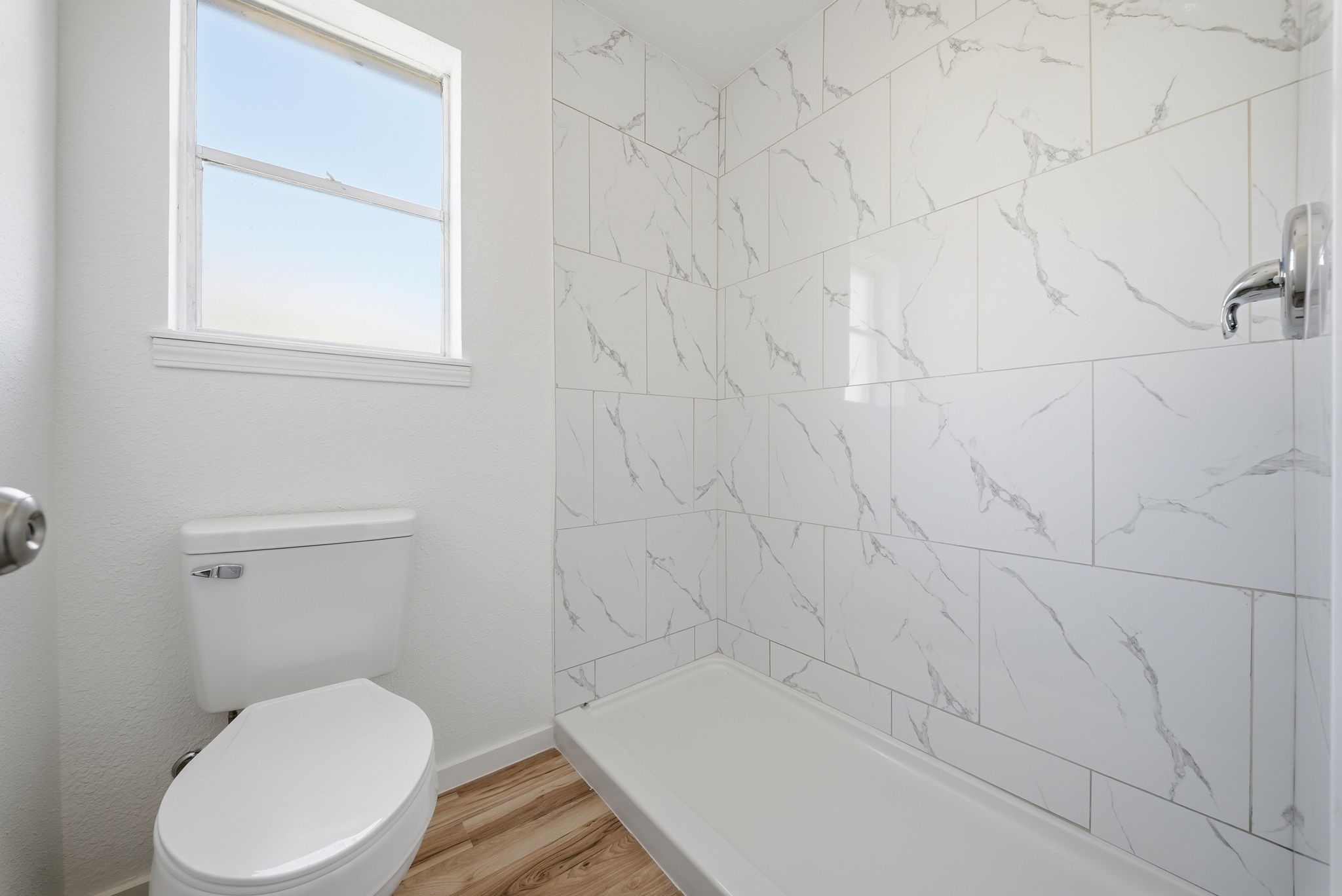 Primary walk-in shower in large marble-look tile, with a window for natural light.