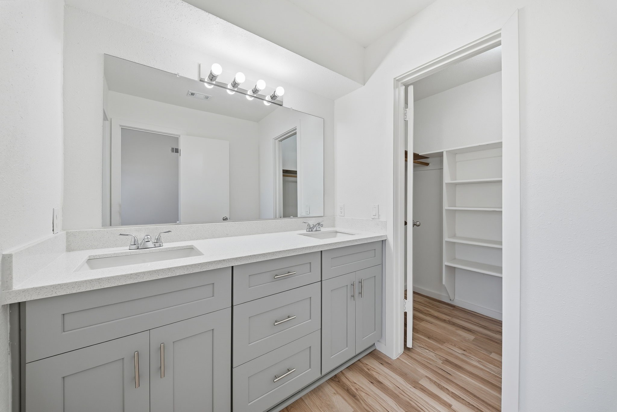 Primary bath double-sink vanity beside a walk-in closet with built-in shelves.