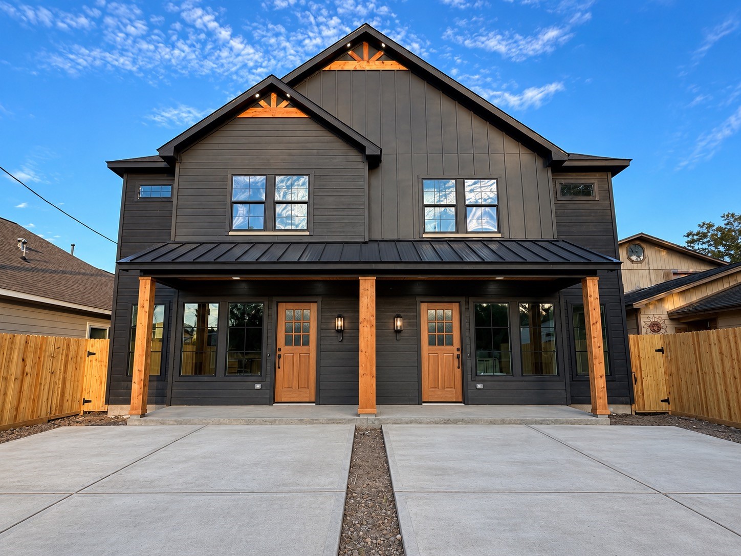 Modern Barn House Duplex with sleek black siding, warm wooden accents, and spacious driveways. This photo has been virtually rendered based on a previous home constructed by the builder. Modern Barn House Duplex with sleek black siding, warm wooden accents, and spacious driveways. This photo has been virtually rendered based on a previous home constructed by the builder.