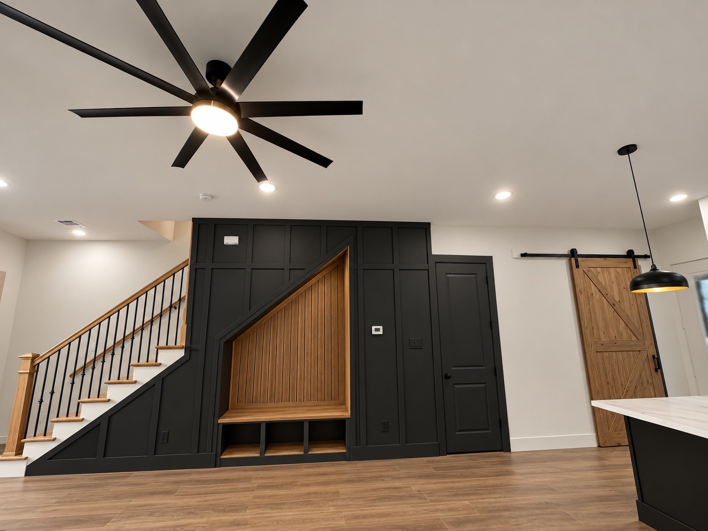 Modern living space featuring a sleek black accent wall with a built in bench, stylish barn door, and elegant staircase with wooden handrails.This photo has been virtually rendered based on the plans for this home.