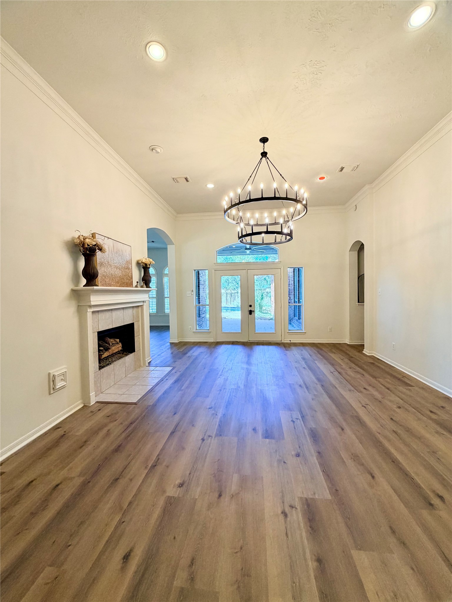 View of the Living room from the foyer. Notice the high ceiling, French doors to the covered patio, recessed lighting, and the gas log fireplace.  The family room is to the left and the Primary bedroom is to the right.