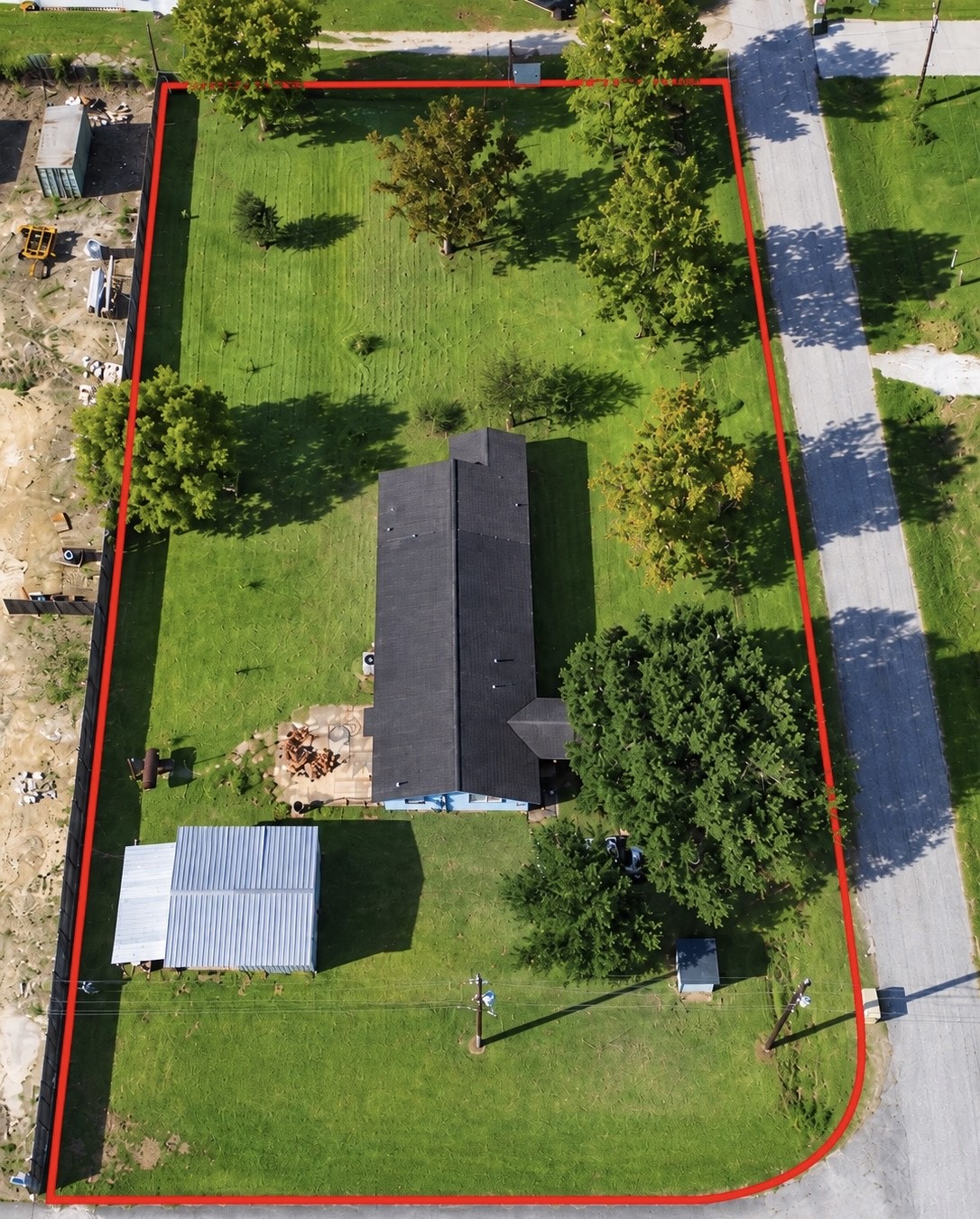Aerial view showcasing the spacious green lawn, mature trees, home, and detached outbuilding. Approximate property boundary outlined in red for reference.