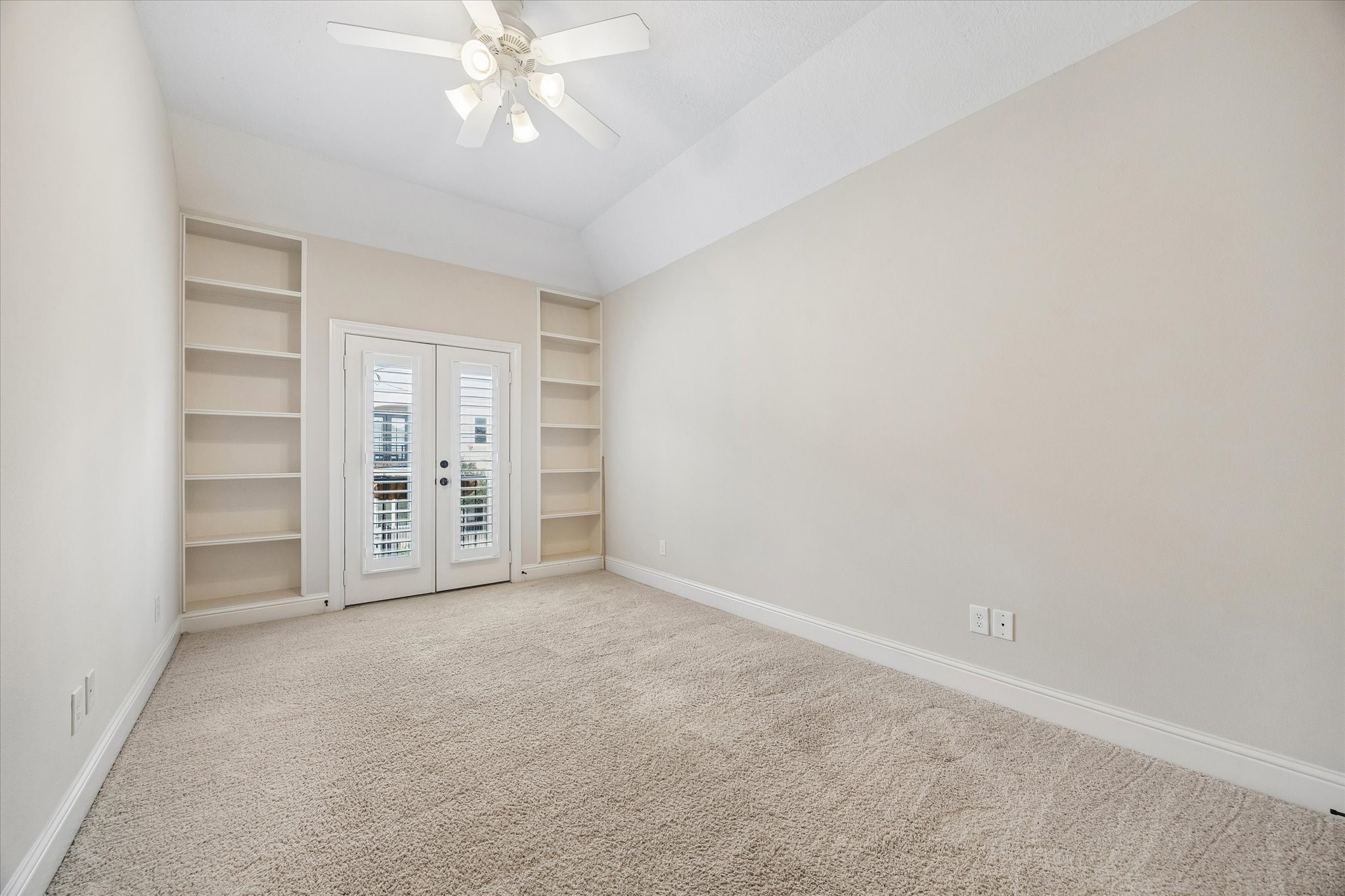 Secondary bedroom with vaulted ceiling, built-in shelving, and private balcony access.