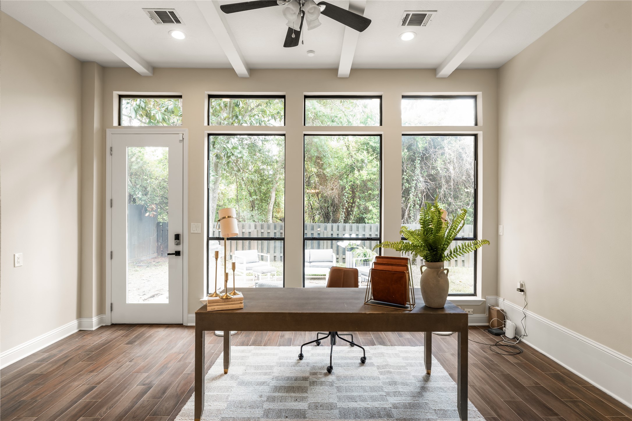 A light filled home office framed by an impressive wall of windows, offering serene backyard views and direct access to the outdoor living area and steps away from the breakfast area.