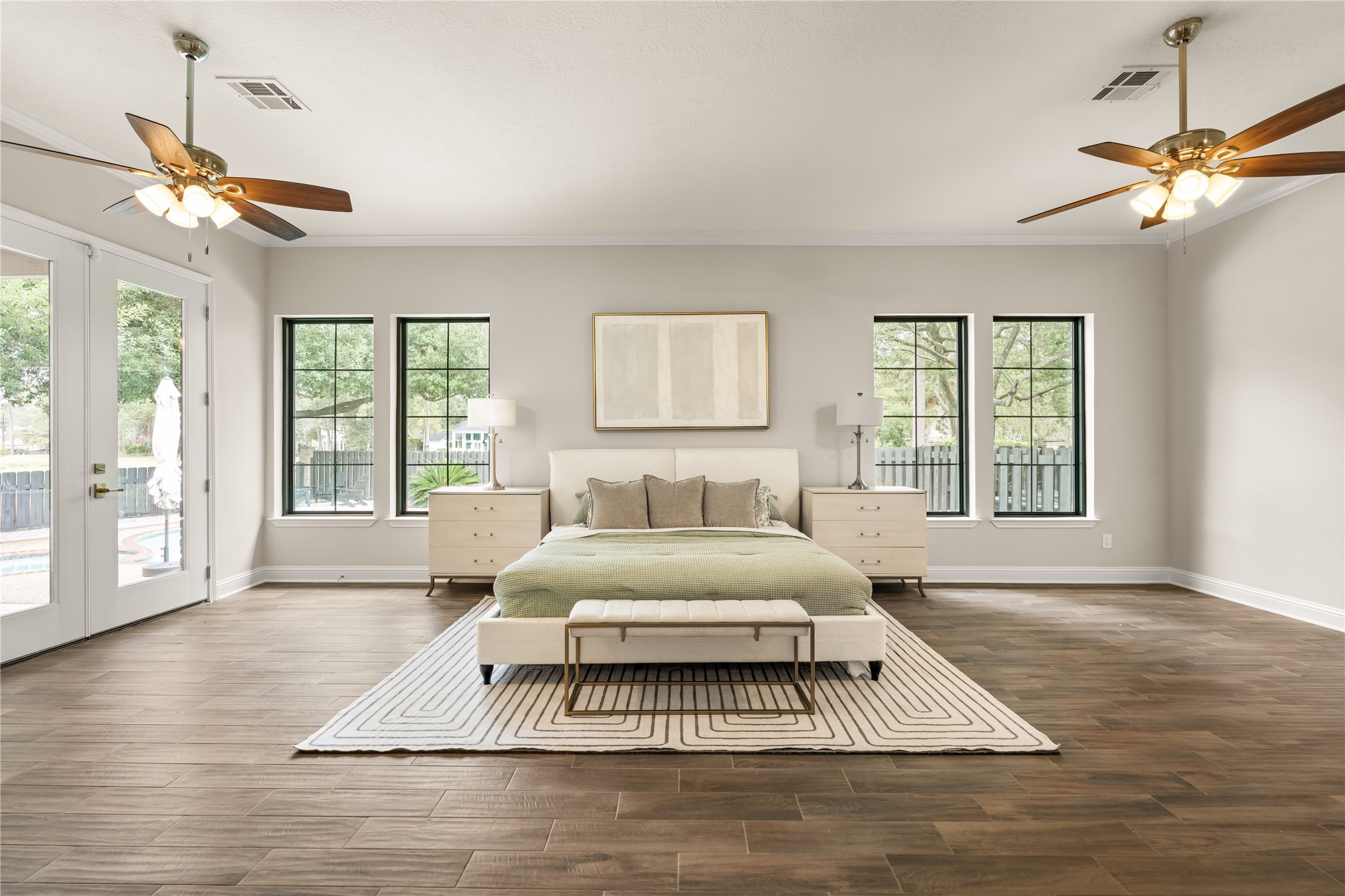 An expansive primary retreat filled with natural light, featuring beautiful wood flooring, multiple windows, and convenient access to the outdoor living area.