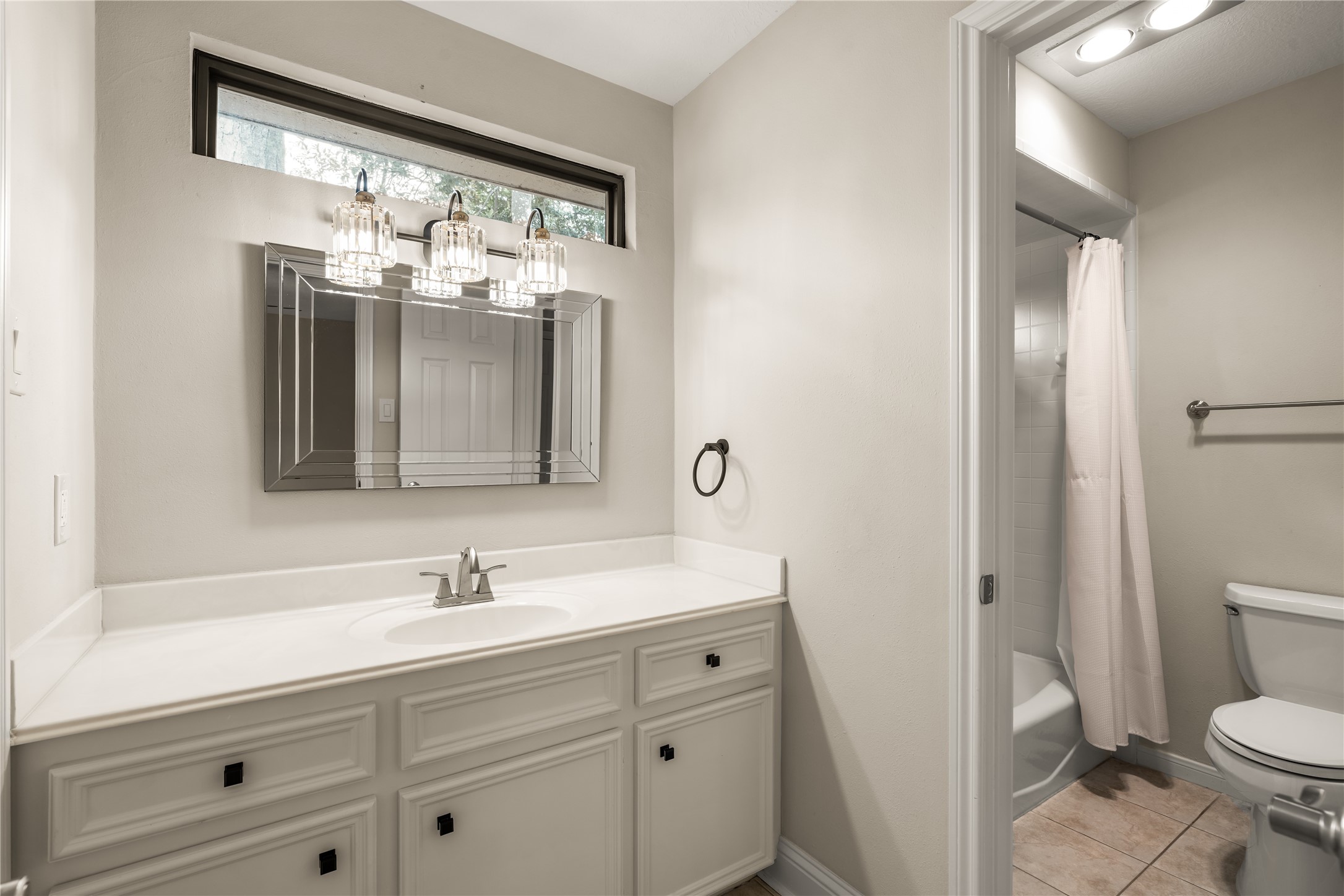 Another secondary bathroom with a polished vanity area, offering generous counter space, ample cabinetry, and an elegant statement mirror, creating a refined and functional space for daily routines.