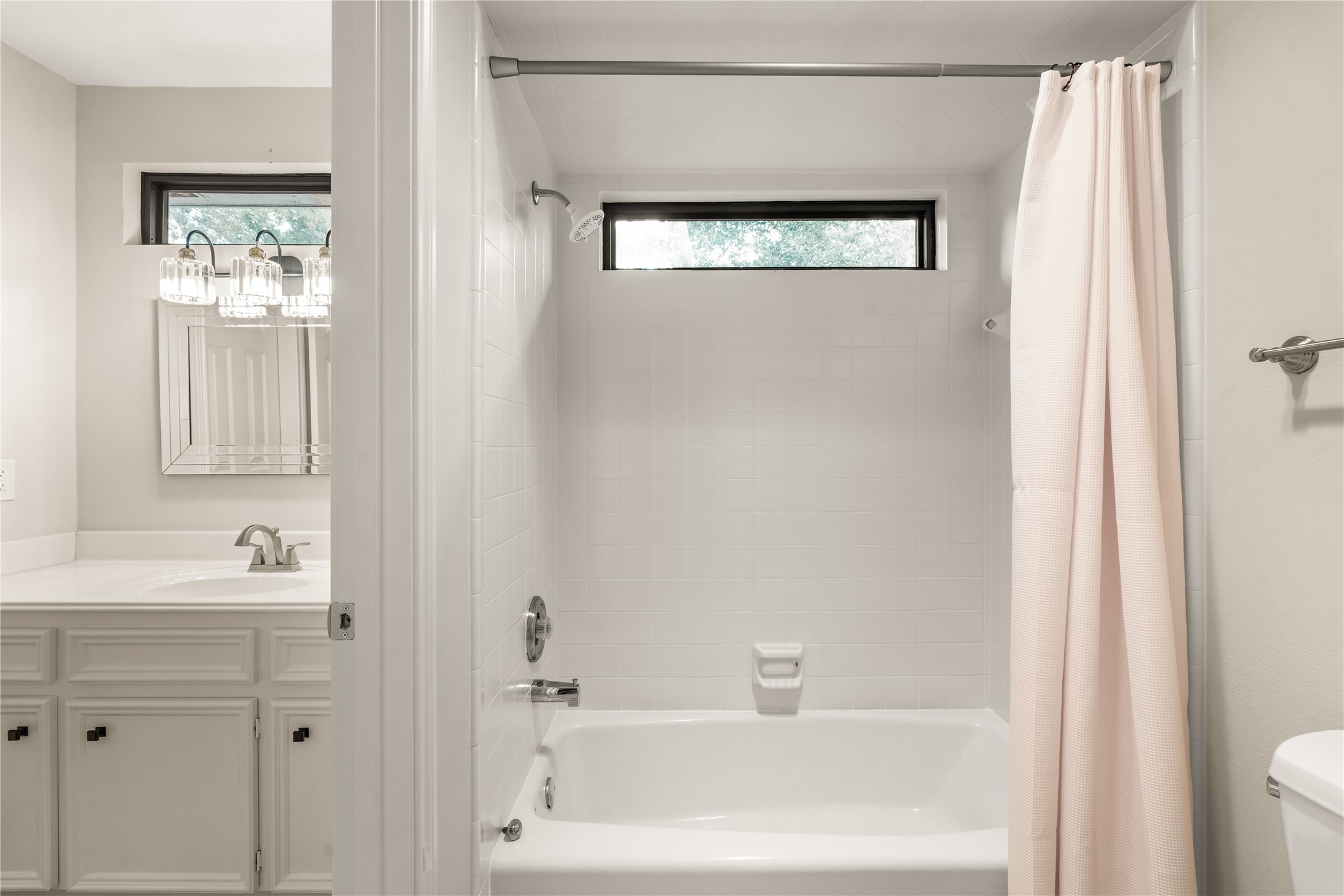 A bright secondary bath features a tub-and-shower combination, crisp tile surround, natural light, and a spacious vanity for comfortable everyday use.