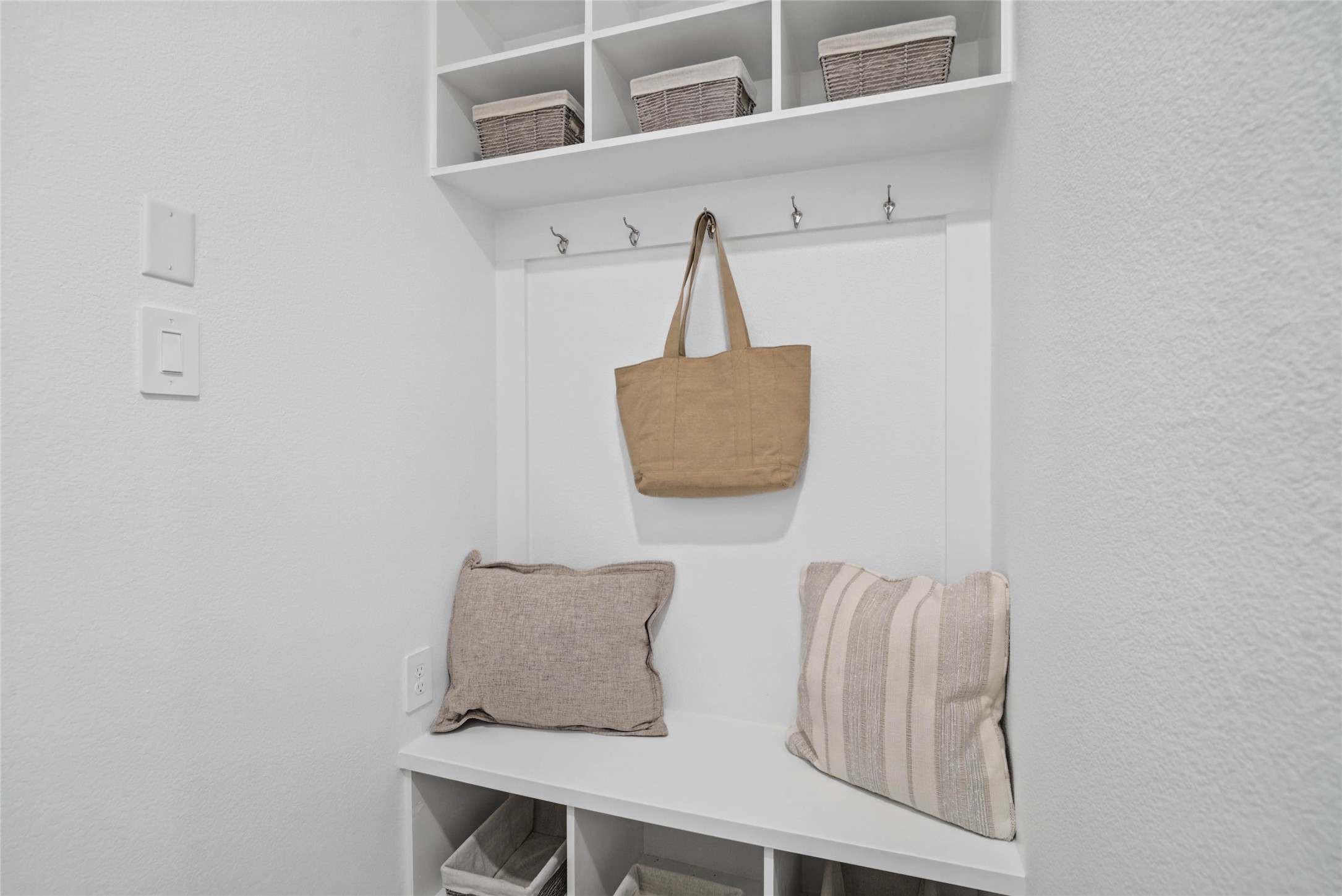 Step into this highly functional and stylish mudroom drop zone, an essential feature for a busy household. The space boasts custom-built white cabinetry and shelving, providing generous storage for coats, bags, and shoes. A comfortable built-in bench offers a convenient spot to sit, while three sleek hooks keep outerwear tidy and accessible.