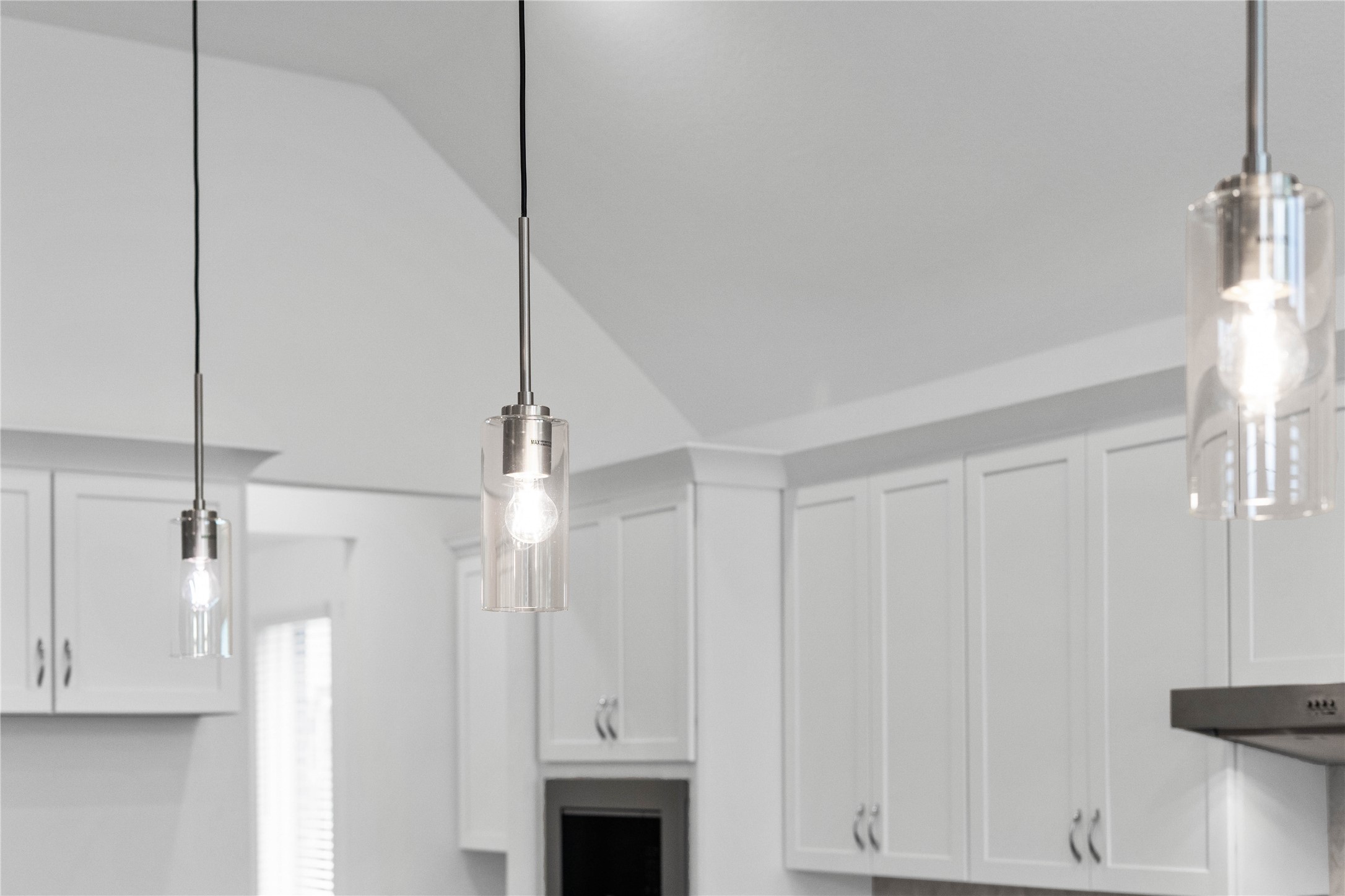 Three exquisite, clear glass pendant lights that elegantly hang above the kitchen island, providing focused task lighting and a touch of refined style.