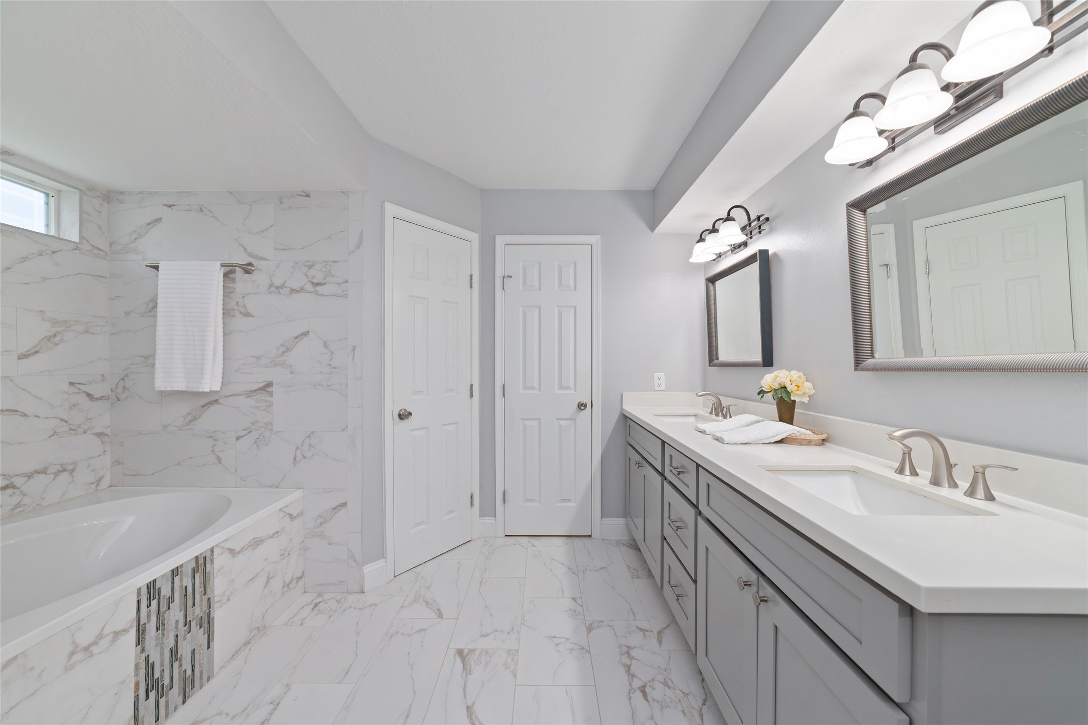 Room to relax, refresh, and recharge! Another view of the spacious Primary Bath showcases the expansive double-sink vanity, generous countertop space, and beautiful marble-look tile flooring. The custom-tiled tub/shower combination adds a touch of elegance, creating a comfortable retreat for everyday routines.