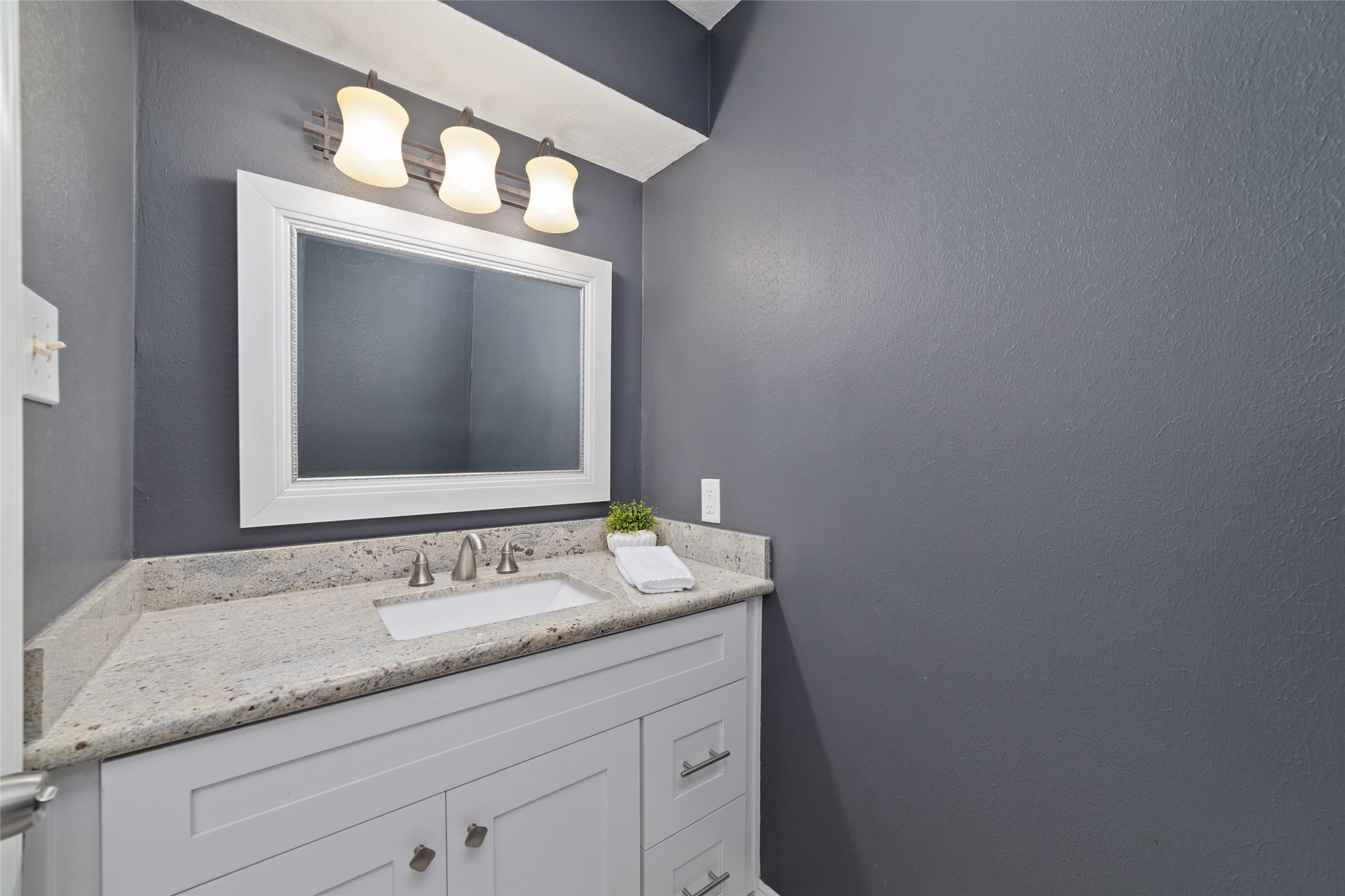 Thoughtfully tucked away from the main living and dining areas, this downstairs Guest Bath offers convenience without sacrificing privacy. A granite-topped vanity, crisp white cabinetry, and rich charcoal walls create a stylish, welcoming space for guests.