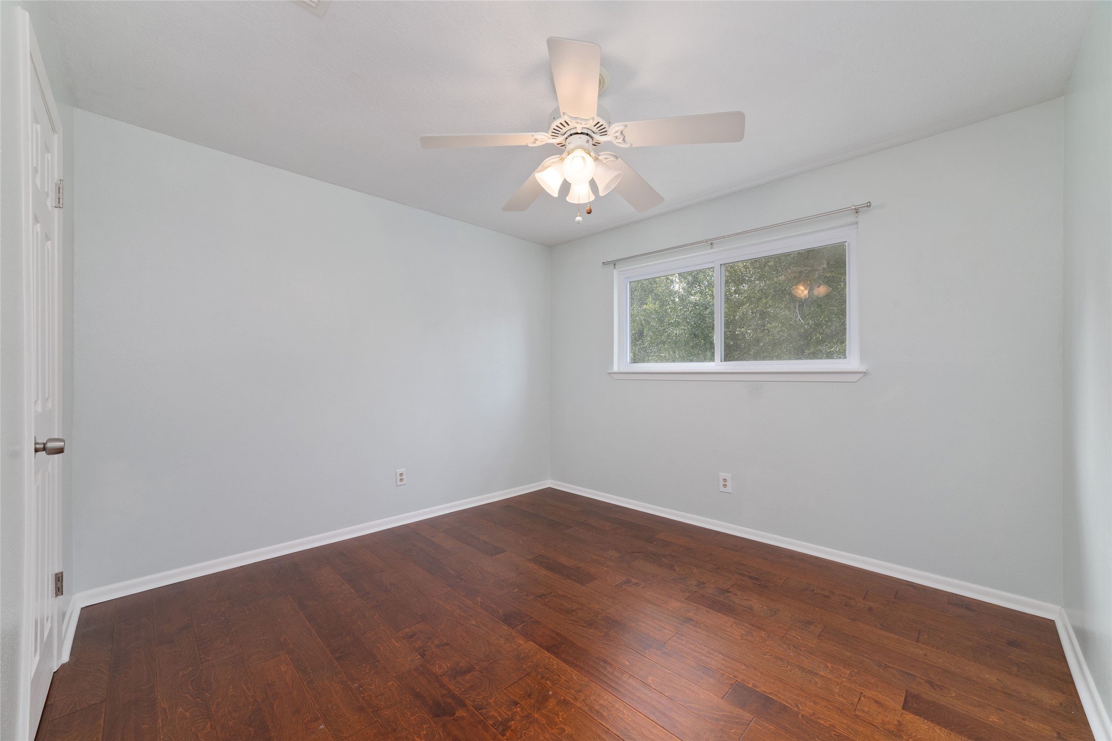 Upstairs secondary bedroom, approximately 11' x 11', features rich wood flooring, a ceiling fan, a large window with views of the backyard, and a walk-in closet. An attached private full bathroom with vanity, sink, and tub/shower combination makes this an inviting retreat for family or guests.