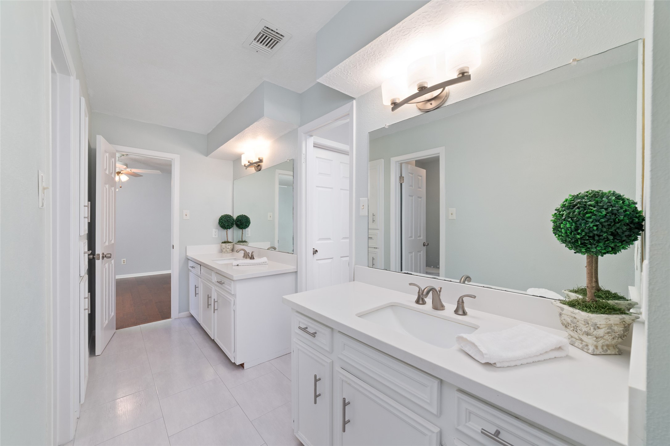 Another view of the spacious Jack-and-Jill bathroom, featuring separate vanity areas with individual sinks, oversized mirrors, and generous cabinet storage. A thoughtfully designed layout provides personal space for each bedroom while sharing a central bathing area