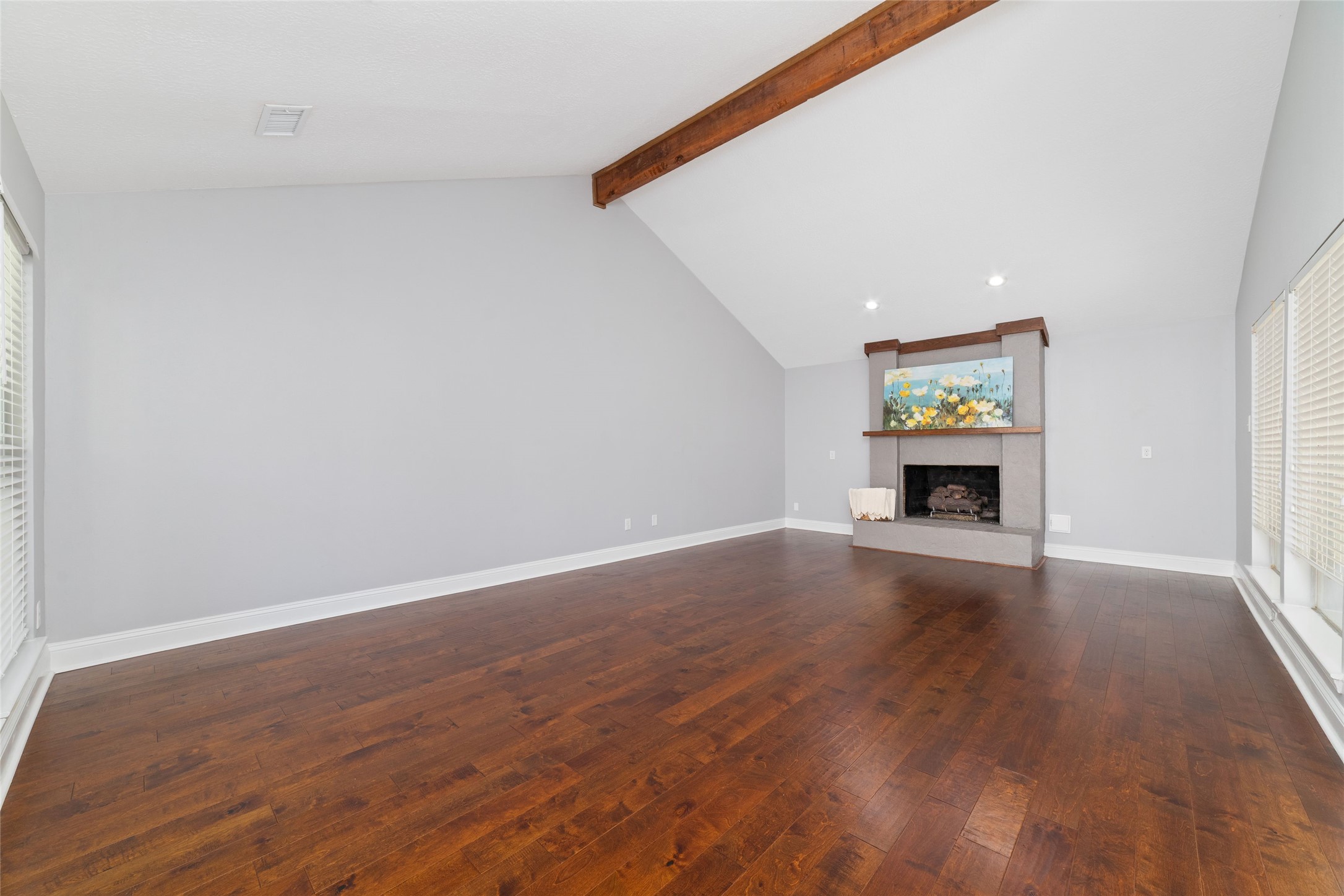Dramatic vaulted ceilings, an exposed wood beam, and rich engineered wood floors bring warmth and architectural character to this spacious Living Room. Expansive windows fill the room with natural light, while a gas log fireplace creates an inviting focal point.