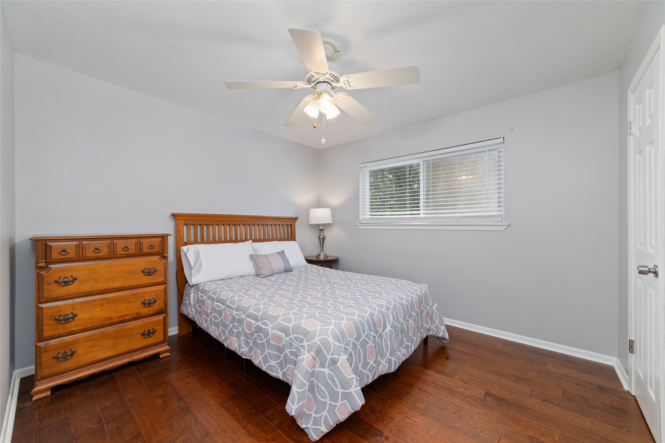 Comfortable upstairs secondary bedroom featuring rich wood floors, a window overlooking the backyard, ceiling fan, and spacious walk-in closet. Plenty of room for bedroom furnishings while maintaining an open, inviting feel