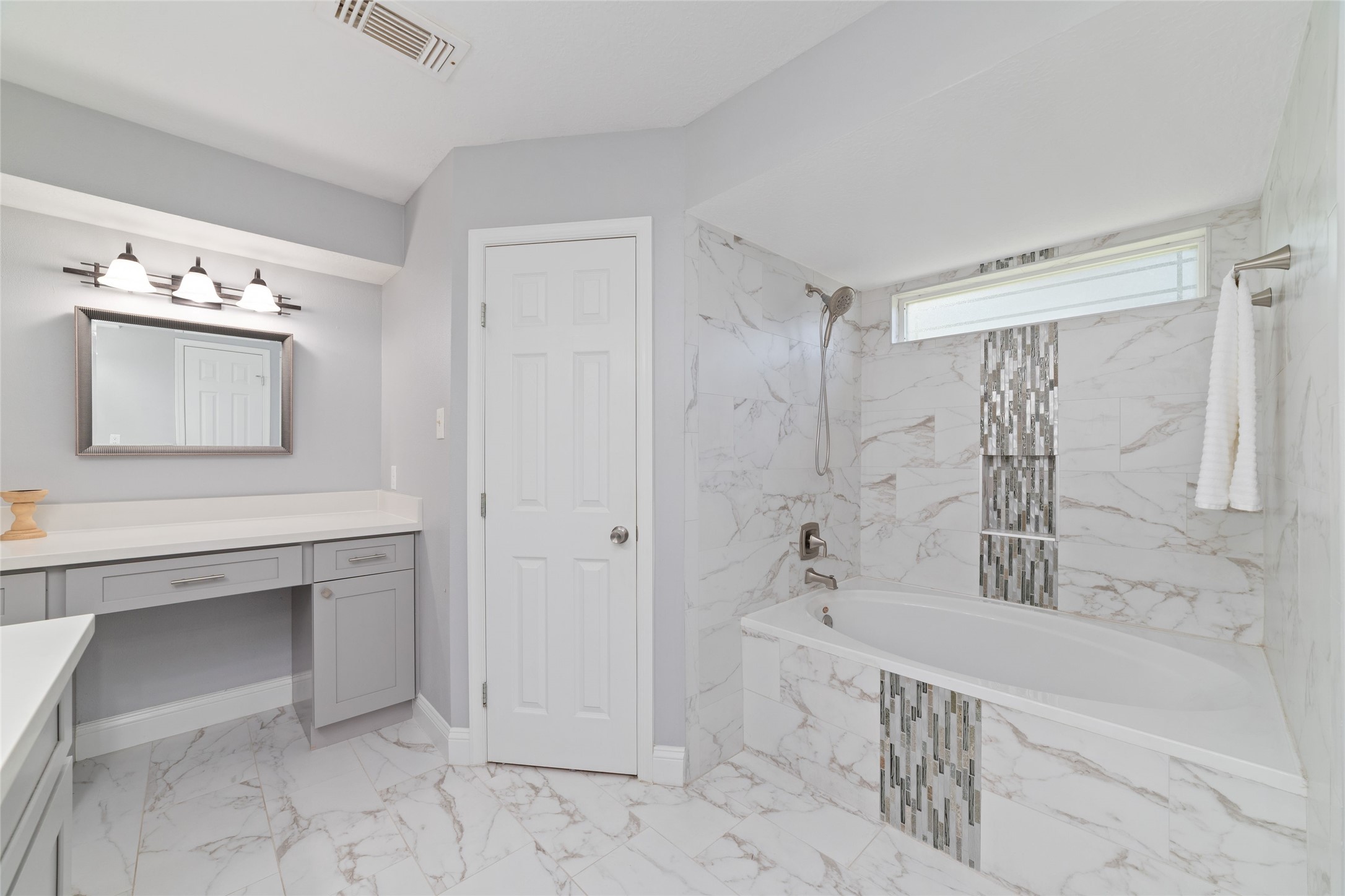 Beautiful details make all the difference! The Primary Bath features a custom-tiled tub/shower combination with elegant glass mosaic accents, a convenient handheld showerhead, and natural light from the window above. A separate seated vanity offers a dedicated space for getting ready, completing this thoughtfully updated retreat.
