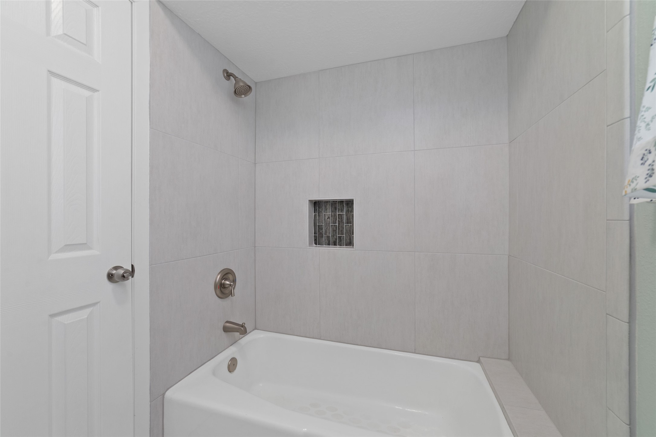 Updated shared tub/shower features a fresh, contemporary tile surround, brushed nickel fixtures, and a recessed shampoo niche with decorative mosaic tile accents