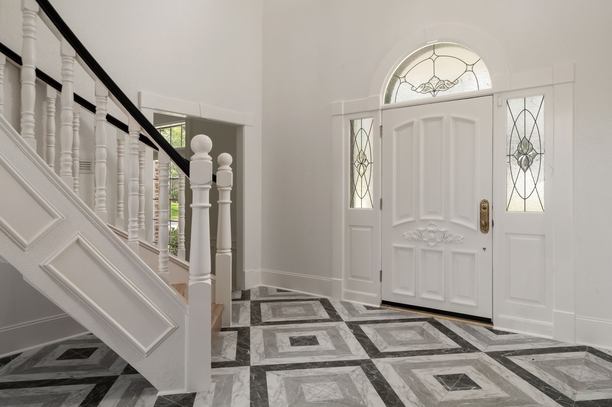 A sweeping curved staircase anchors the two-story entry, creating a dramatic first impression upon arrival. Patterned tile flooring, oversized windows, and a renovated interior enhance the foyers architectural scale and natural light. Open sightlines connect the entry to the homes main living spaces.