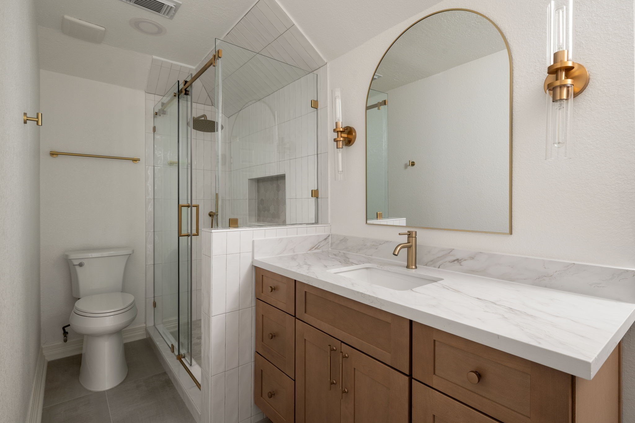 Secondary bathrooms combine updated cabinetry, contemporary fixtures, and frameless glass shower enclosures within clean, modern layouts. Quartz surfaces and designer lighting add contrast and texture throughout the spaces. Functional storage and updated finishes enhance everyday usability.