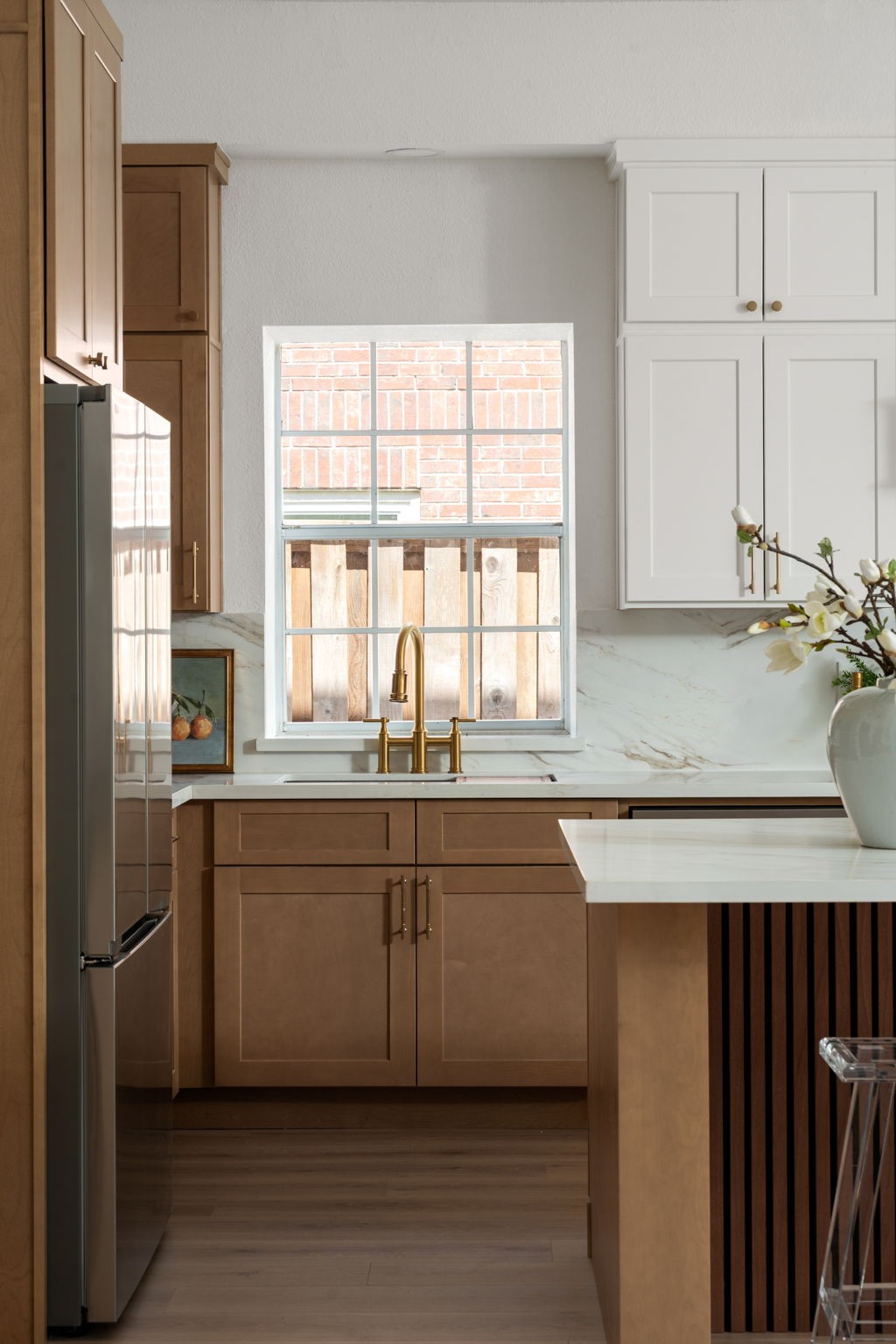 Large windows bring natural light into the kitchen while highlighting the updated finishes and custom cabinetry. Quartz countertops, brass fixtures, and integrated storage contribute to the kitchens modern functionality. The layout was designed to maintain connection to the homes main entertaining spaces.