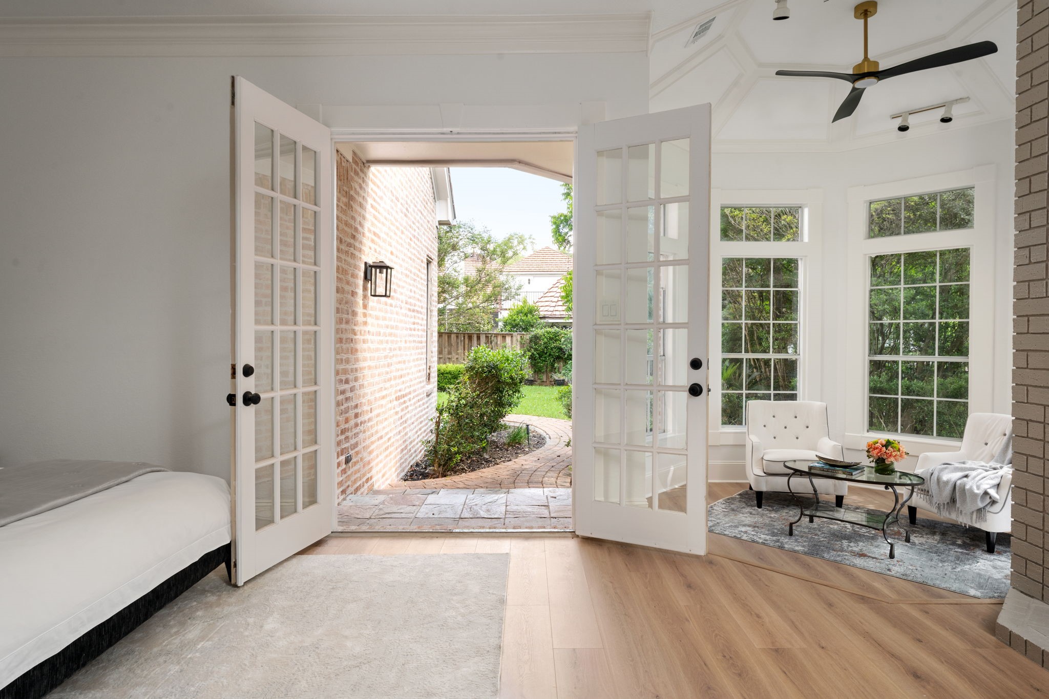 Positioned within its own private wing, the primary suite offers strong indoor-outdoor connection through expansive windows and direct patio access. The layout includes additional space for seating or lounge areas near the decorative fireplace feature. Contemporary finishes and updated flooring continue throughout the room.