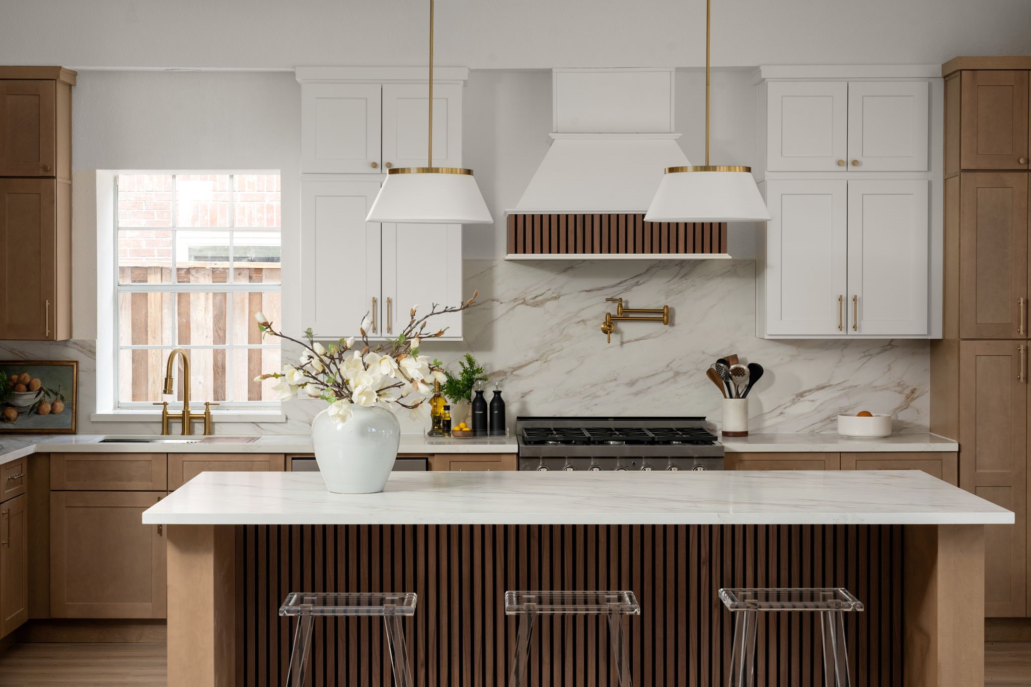 The renovated kitchen centers around an oversized island, designer pendant lighting, and a custom vent hood that creates a clean architectural focal point. Quartz surfaces and integrated storage continue throughout the space. Open transitions connect the kitchen seamlessly to the surrounding entertaining areas.