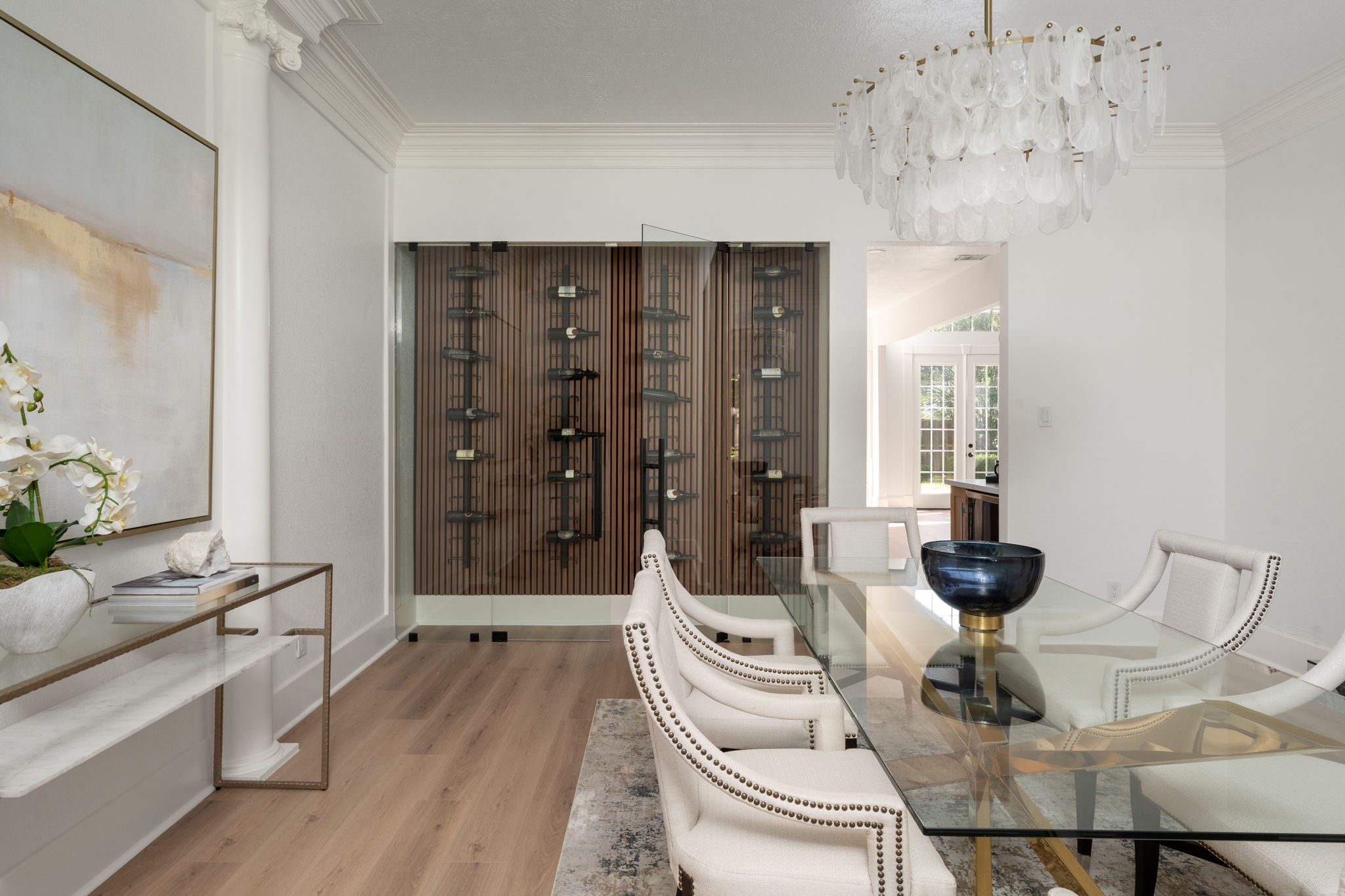 A glass-enclosed wine display creates a striking focal point within the formal dining area and adds a custom entertaining feature to the space. Contemporary lighting, updated finishes, and detailed millwork contribute to the rooms refined atmosphere. Positioned near the foyer, the dining area transitions seamlessly into the surrounding living spaces.