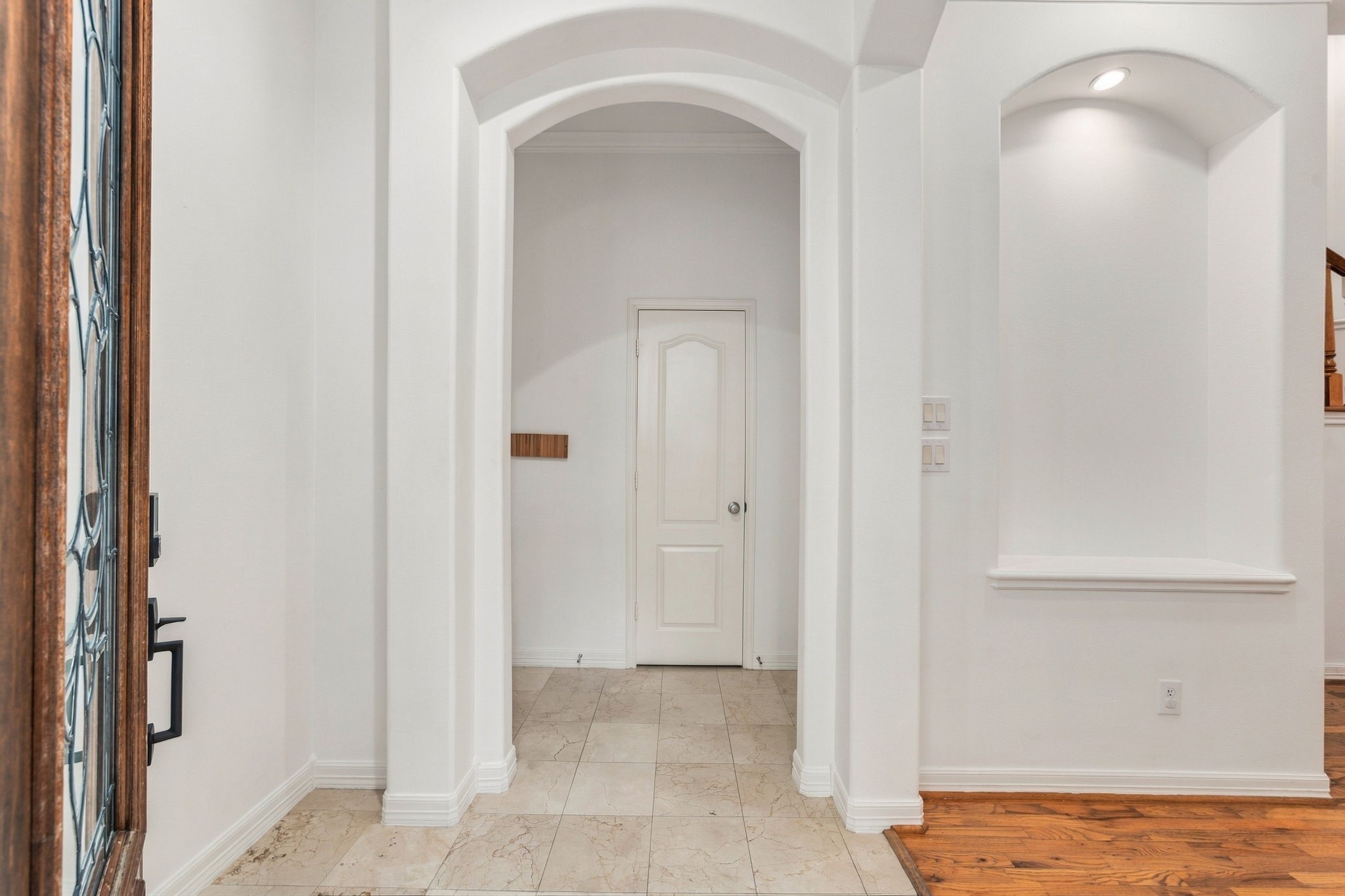 A welcoming entry featuring graceful archways, a decorative front door & elegant crown molding, with a combination of tile & hardwood flooring that adds warmth and character to the home.